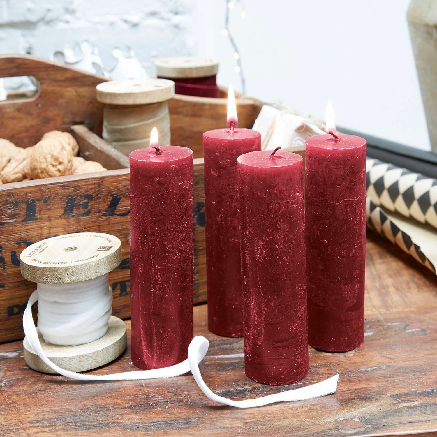 Set de 4 velas Muriel Cuatro velas rojas de cera sobre mesa de madera con carretes decorativos y nueces