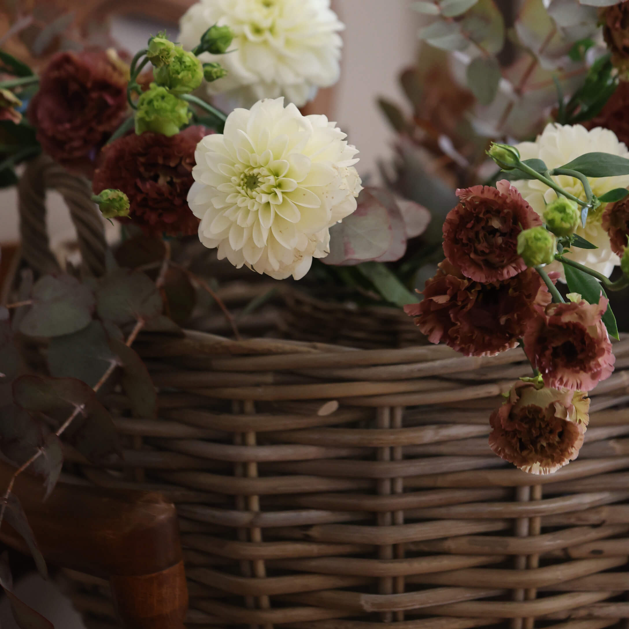 Ramo de flores crema y burdeos en cesta de mimbre para decoración interior