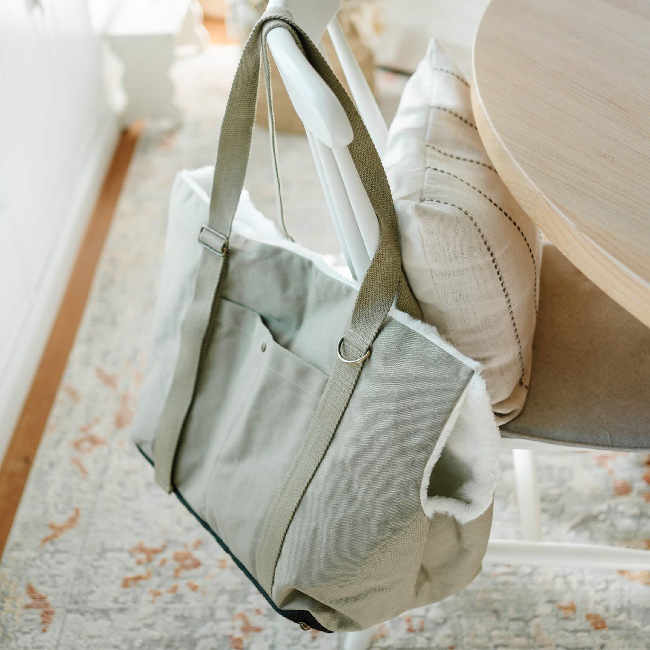Bolsa gris de tela con interior de piel blanca colgada de una silla blanca en una habitación luminosa