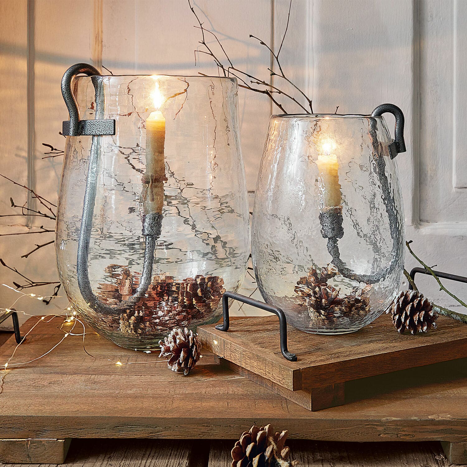 Set de 2 portavelas Lorcalla Dos faroles de vidrio transparente con asas de metal y velas, decorados con piñas