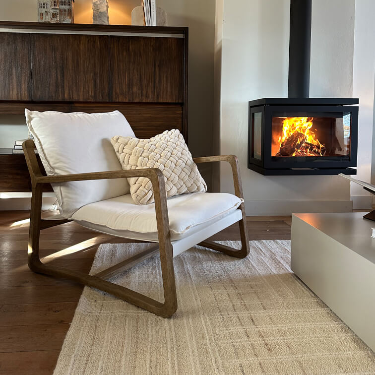 Sillón de madera con cojín blanco junto a chimenea moderna en sala acogedora