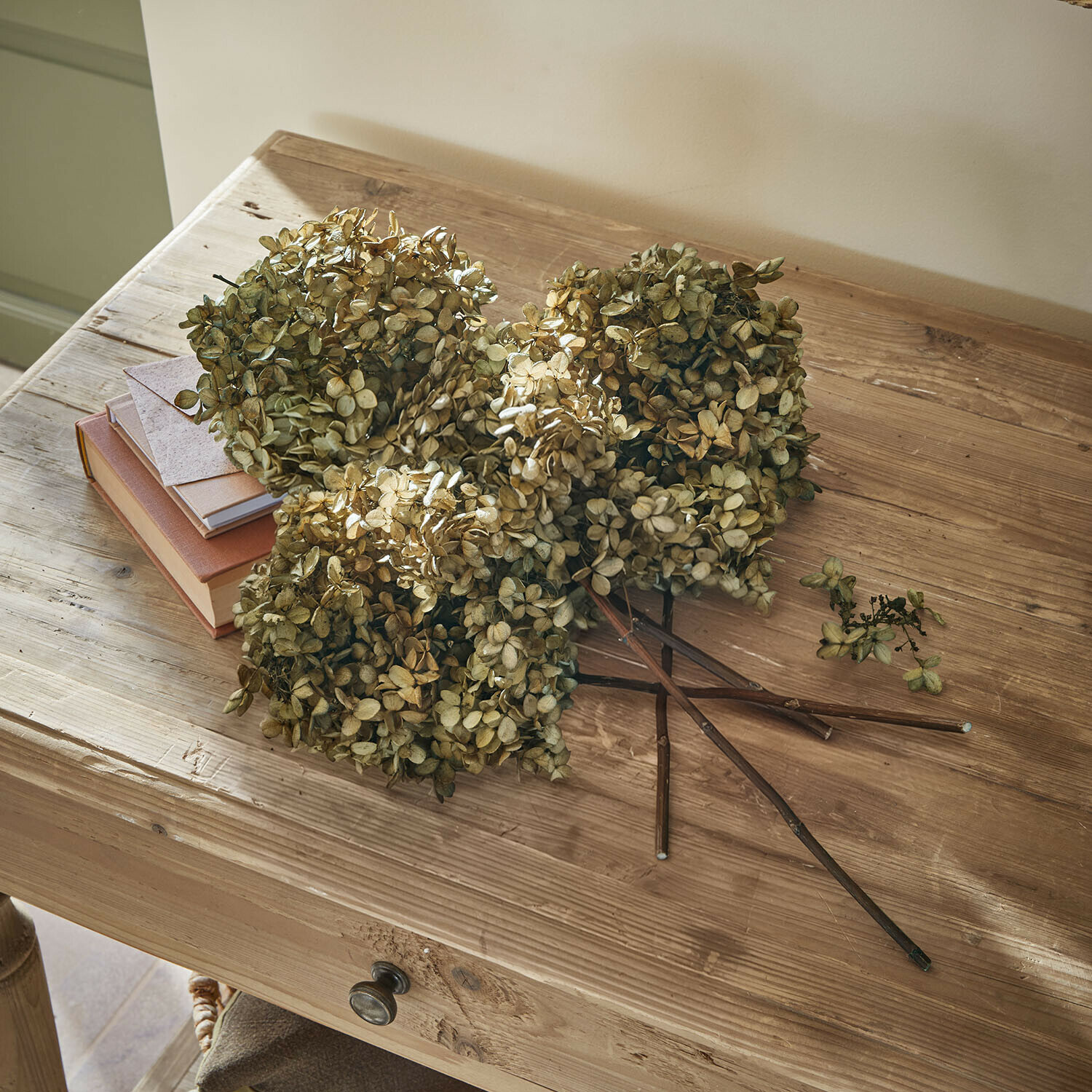 Flores secas de hortensia beige sobre mesa de madera con libros y un sobre