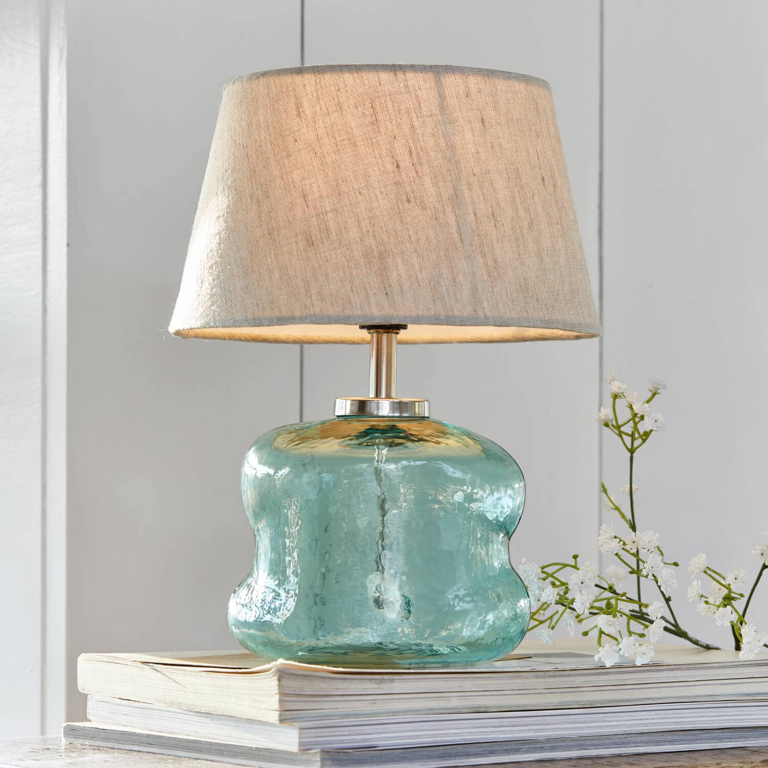 Lámpara de mesa de vidrio azul con pantalla beige sobre libros, decoración para interiores