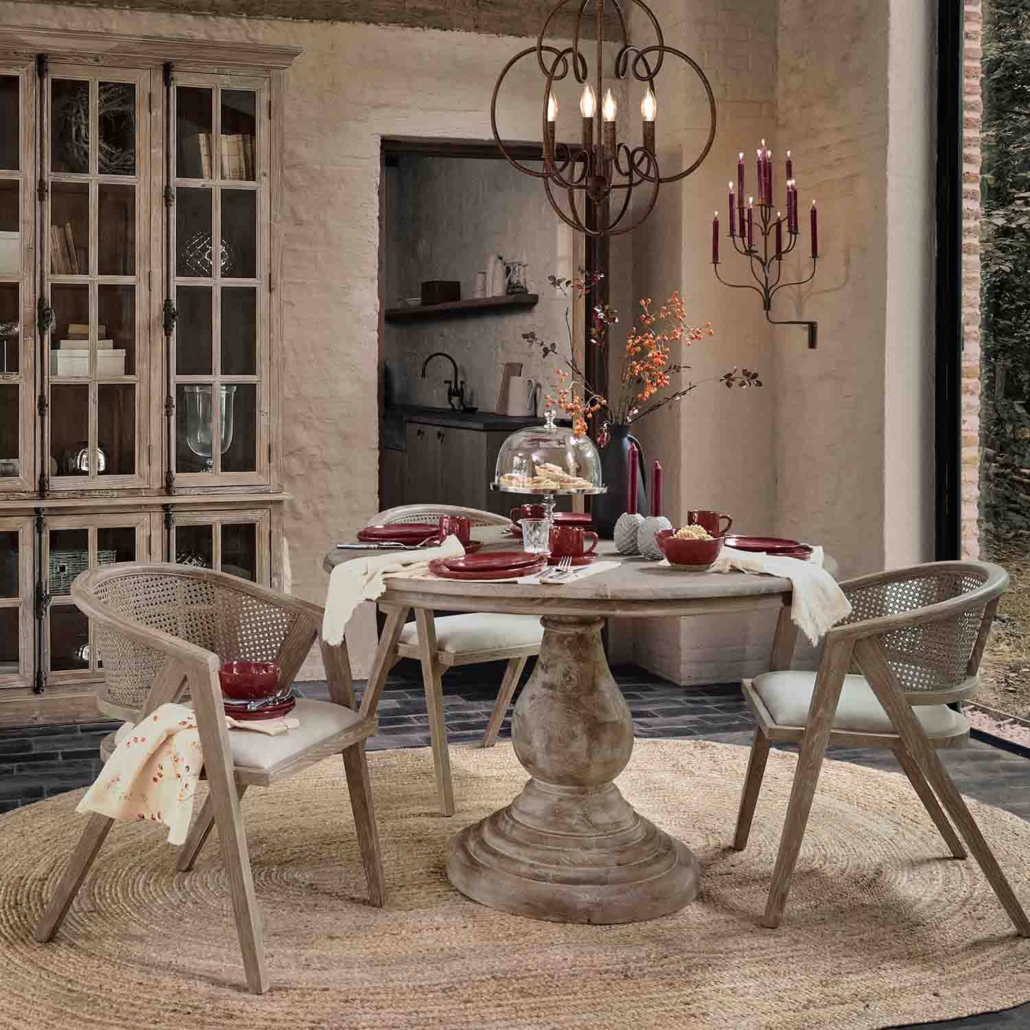 Comedor con mesa redonda de madera y sillas de ratán en tonos naturales, decoración en color burdeos