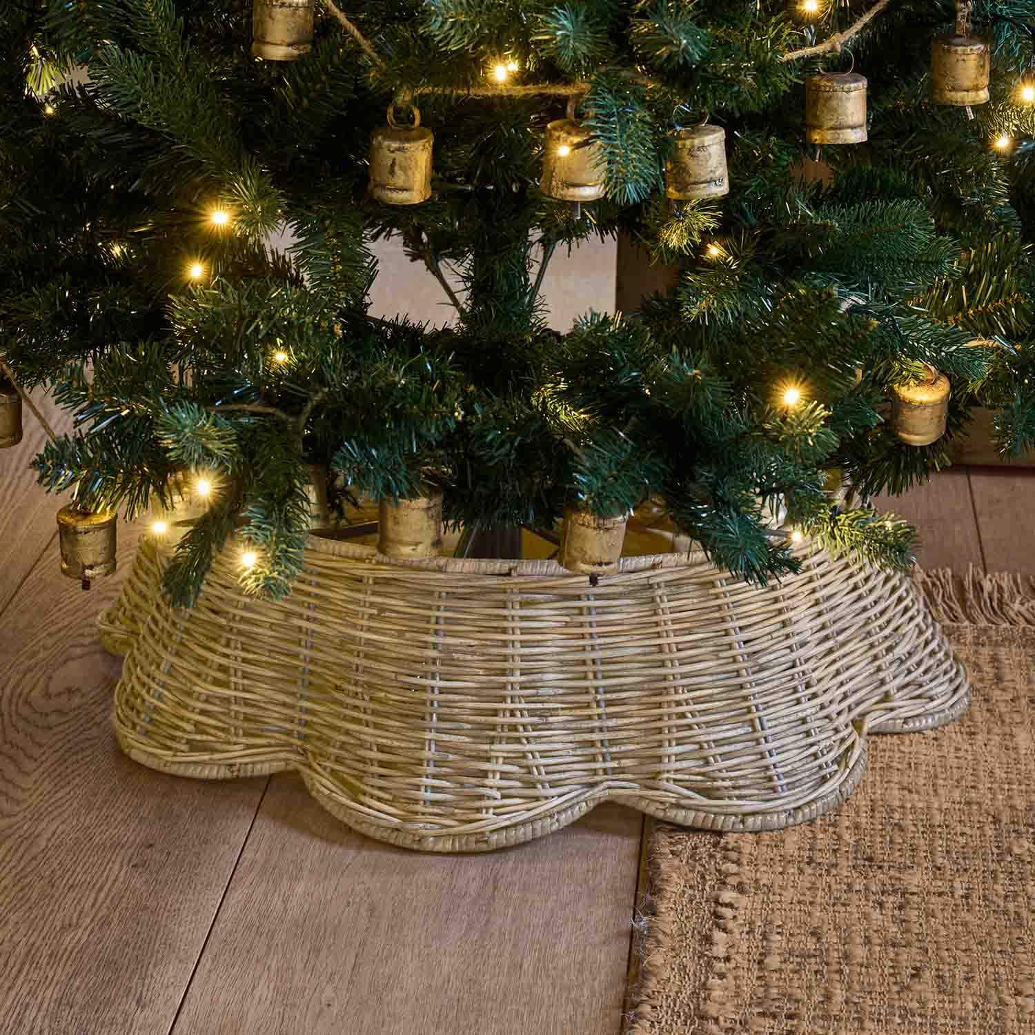 Base de mimbre natural color beige claro bajo un árbol de Navidad verde con luces cálidas