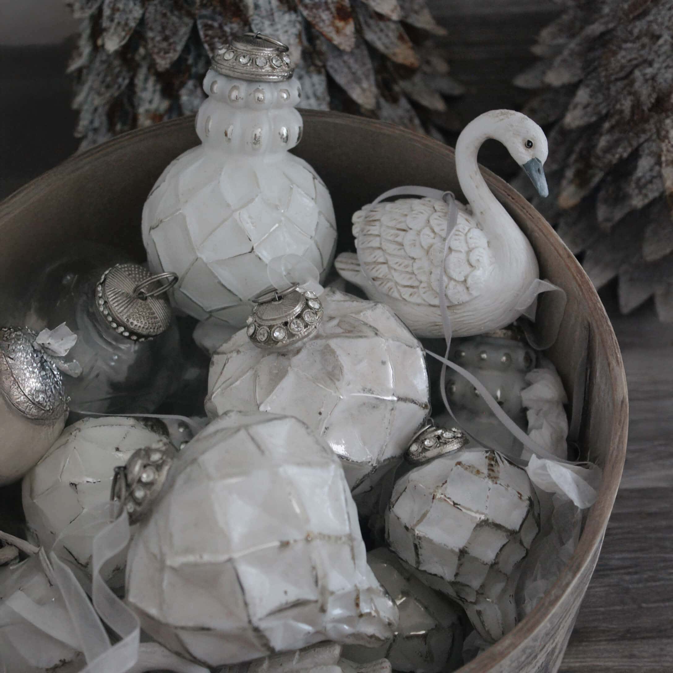 Adornos navideños blancos de cerámica y vidrio en un cuenco de madera, decoraciones invernales