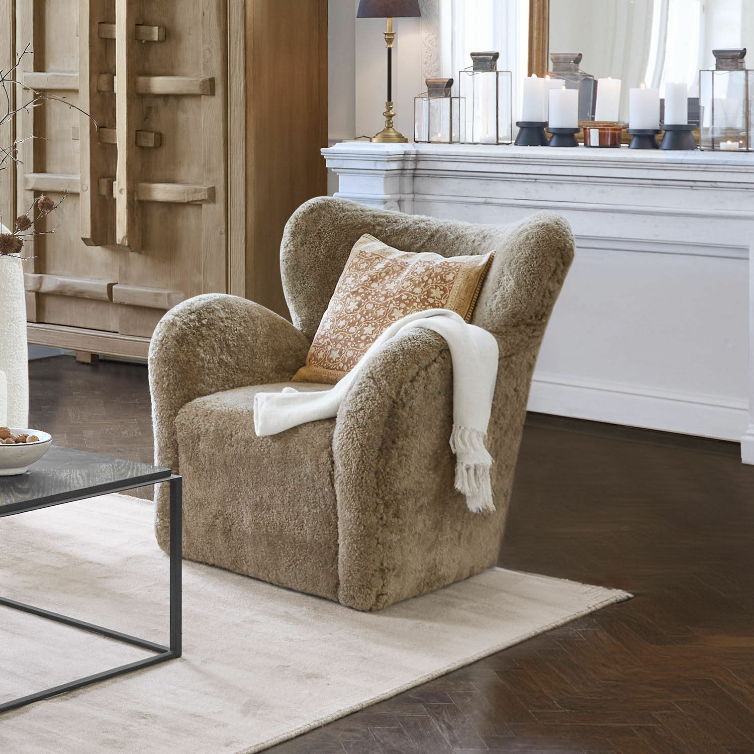 Sillón beige de material suave con cojín y manta blanca en sala de estar elegante