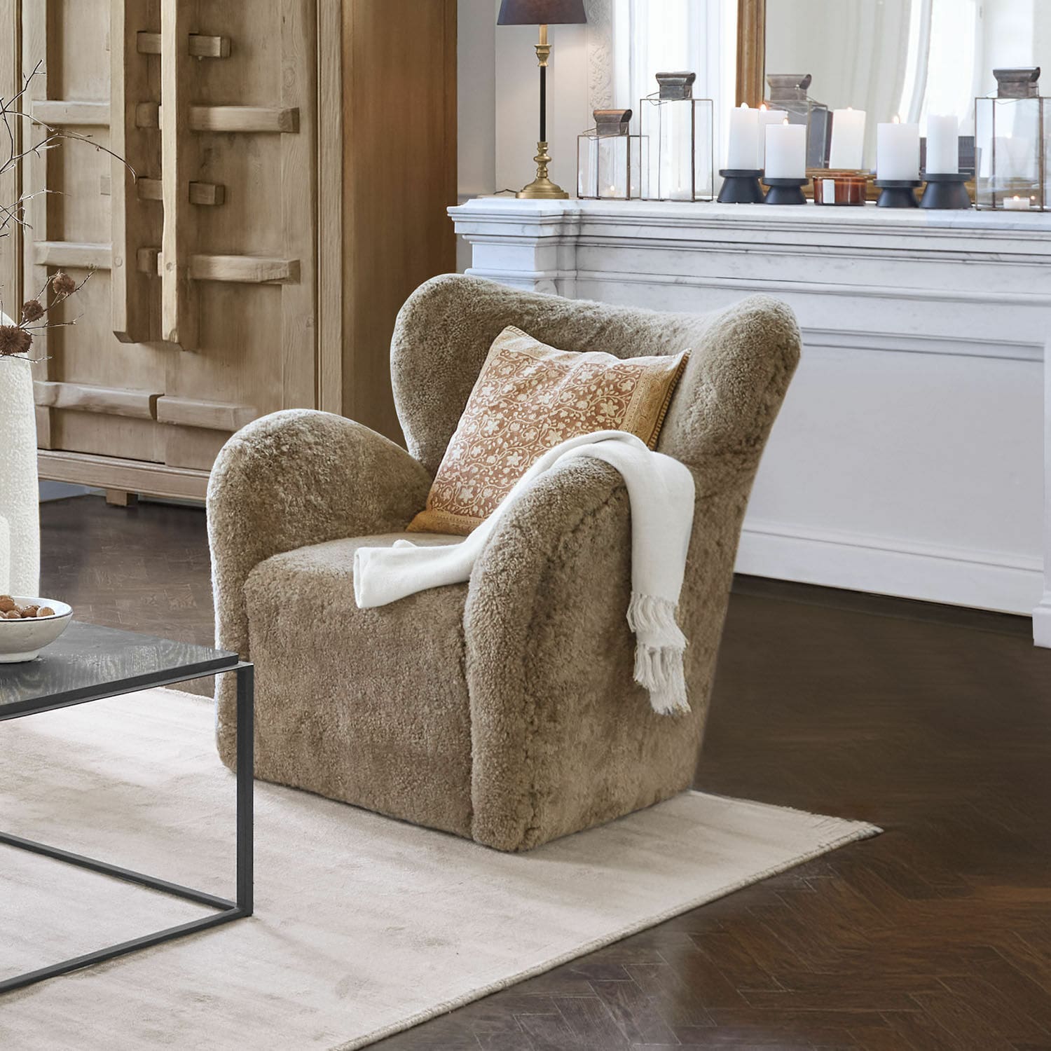 Sillón Ambrécourt Sillón beige de material suave con cojín y manta blanca en sala de estar elegante