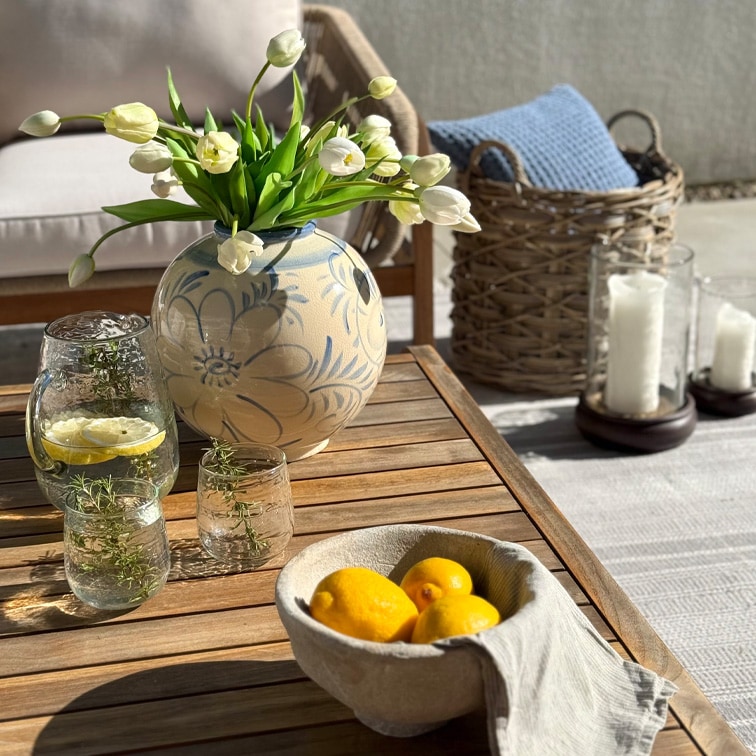 Jarrón decorativo de cerámica con diseño floral y tulipanes blancos sobre mesa de madera en terraza