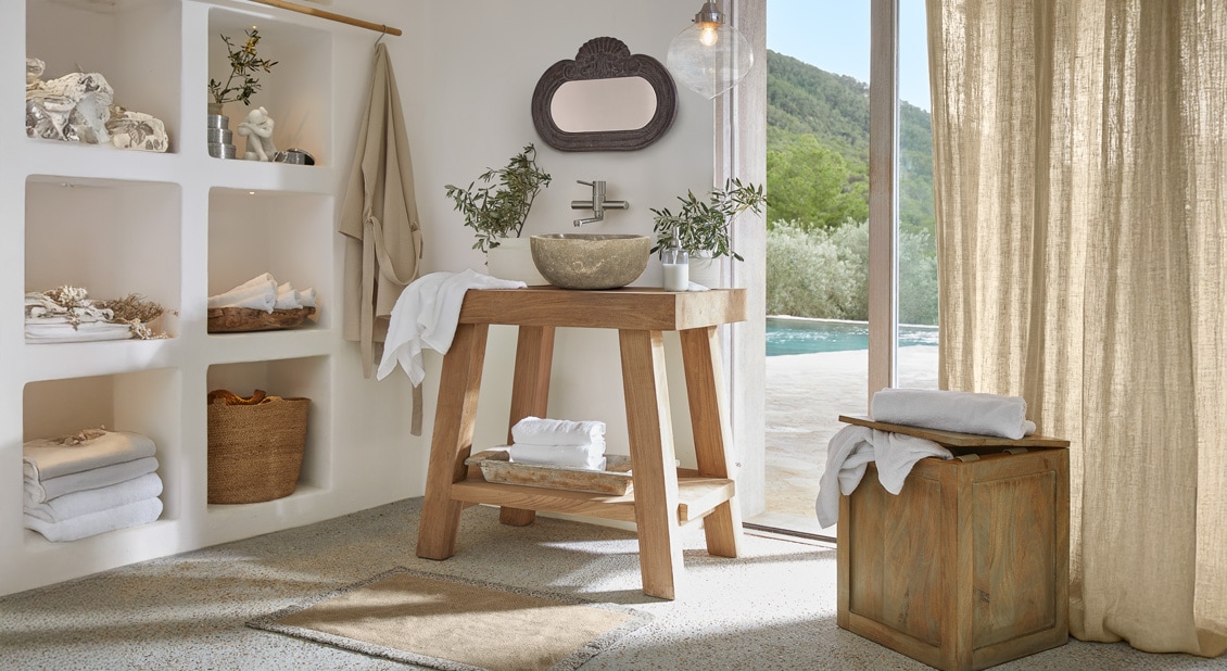 Baño con lavabo de madera y cuenca de piedra, luz natural y accesorios beige