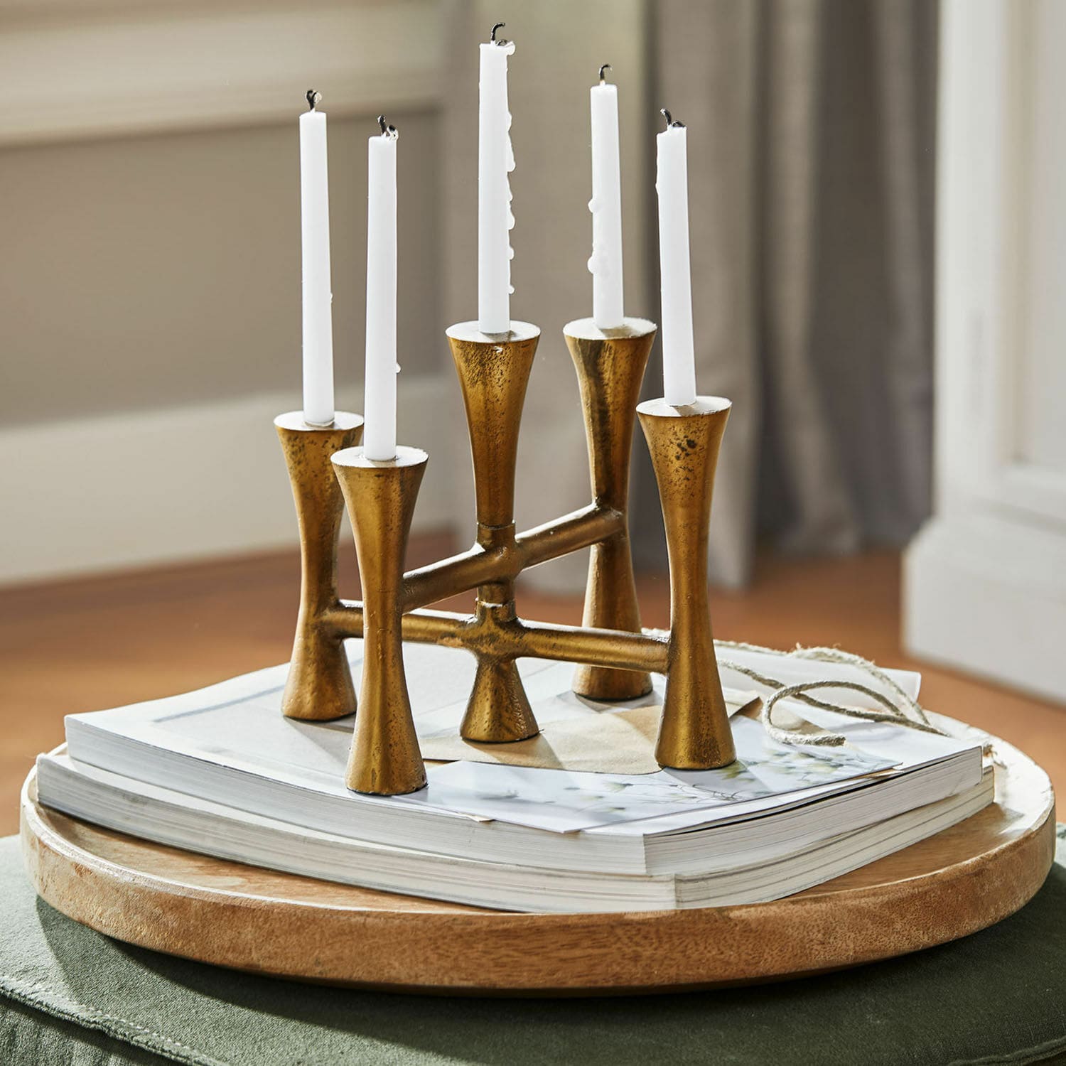 Candelabro dorado de metal para cinco velas blancas sobre bandeja de madera con libros, decoración interior