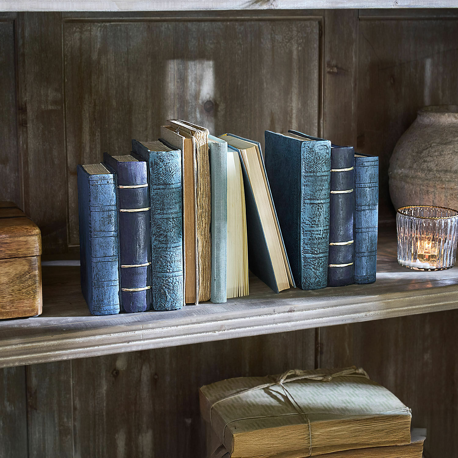 Set de 2 sujetalibros Morvini Conjunto de libros antiguos con cubiertas azules y beige en estantería de madera junto a un portavelas