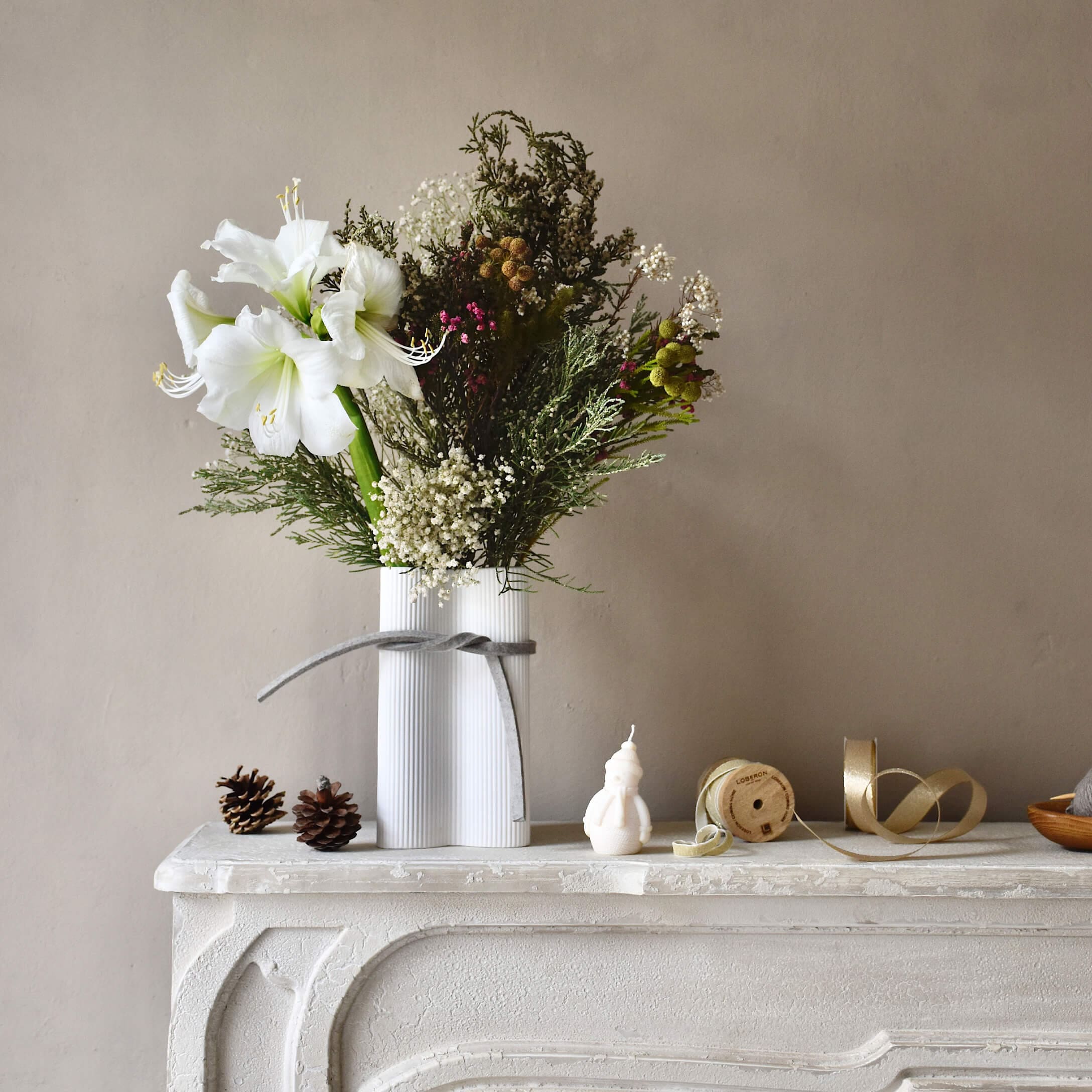 Jarrón de cerámica blanca con flores blancas y ramas verdes sobre una chimenea blanca decorativa