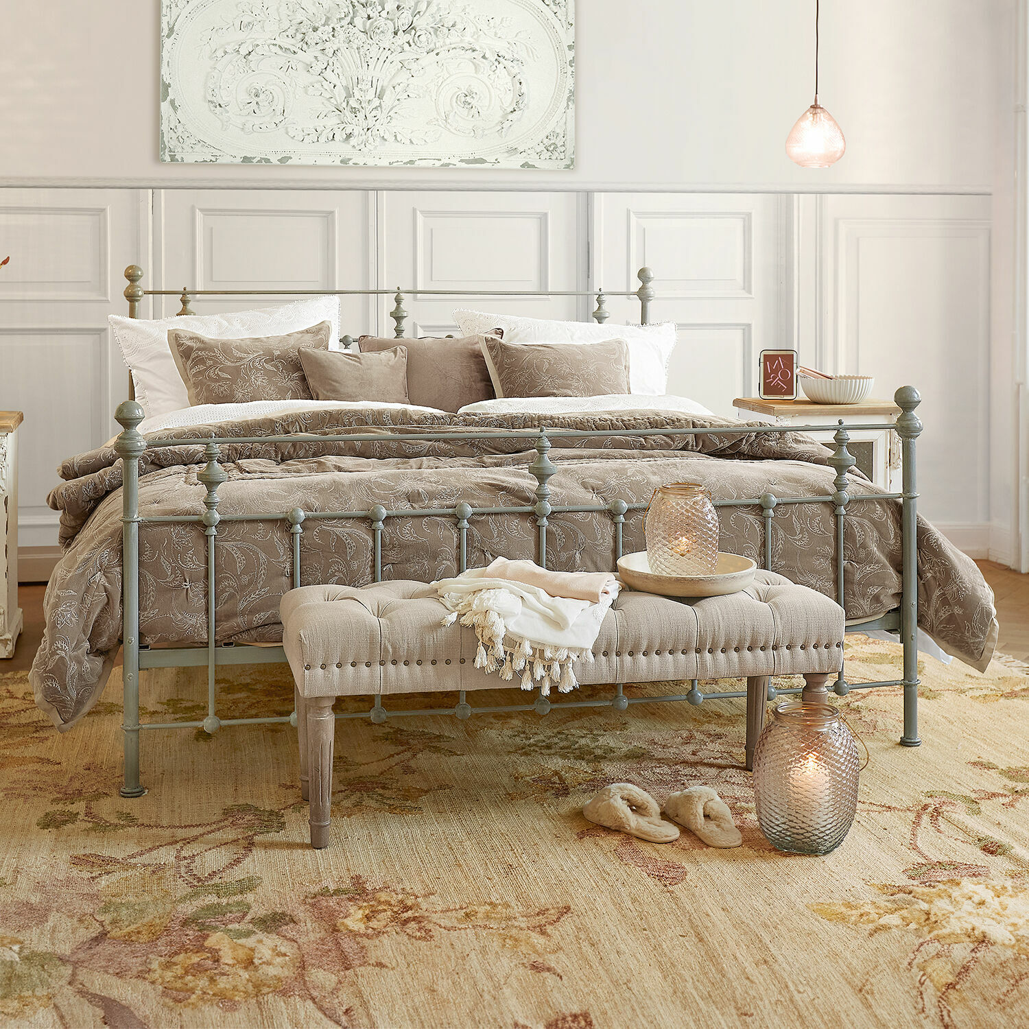 Cama Beauvierre Dormitorio con cama metálica gris, ropa de cama beige con diseño floral y banco acolchado al pie de la cama