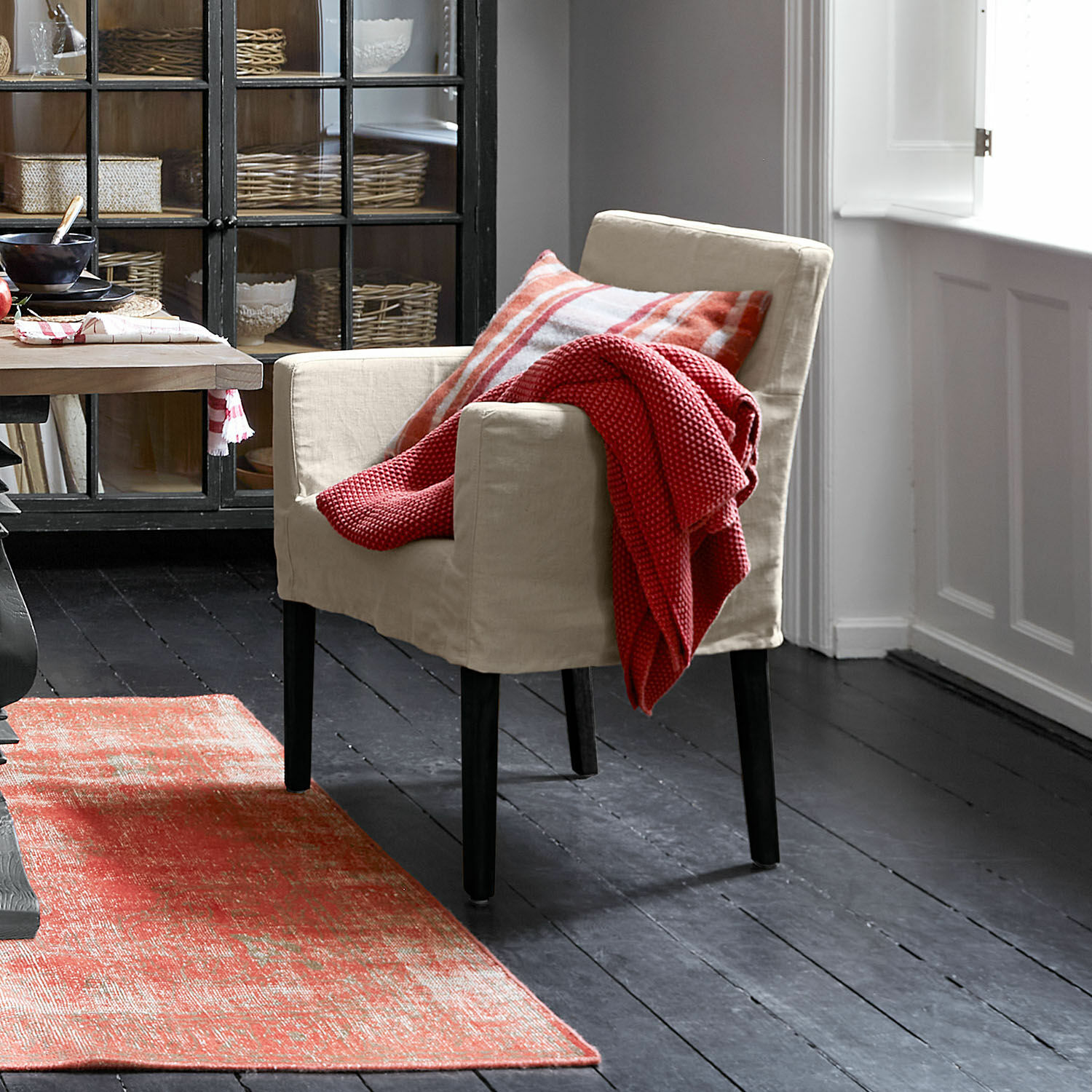 Silla Longhill Sillón beige de tela con patas negras, manta roja y cojín a cuadros, alfombra roja