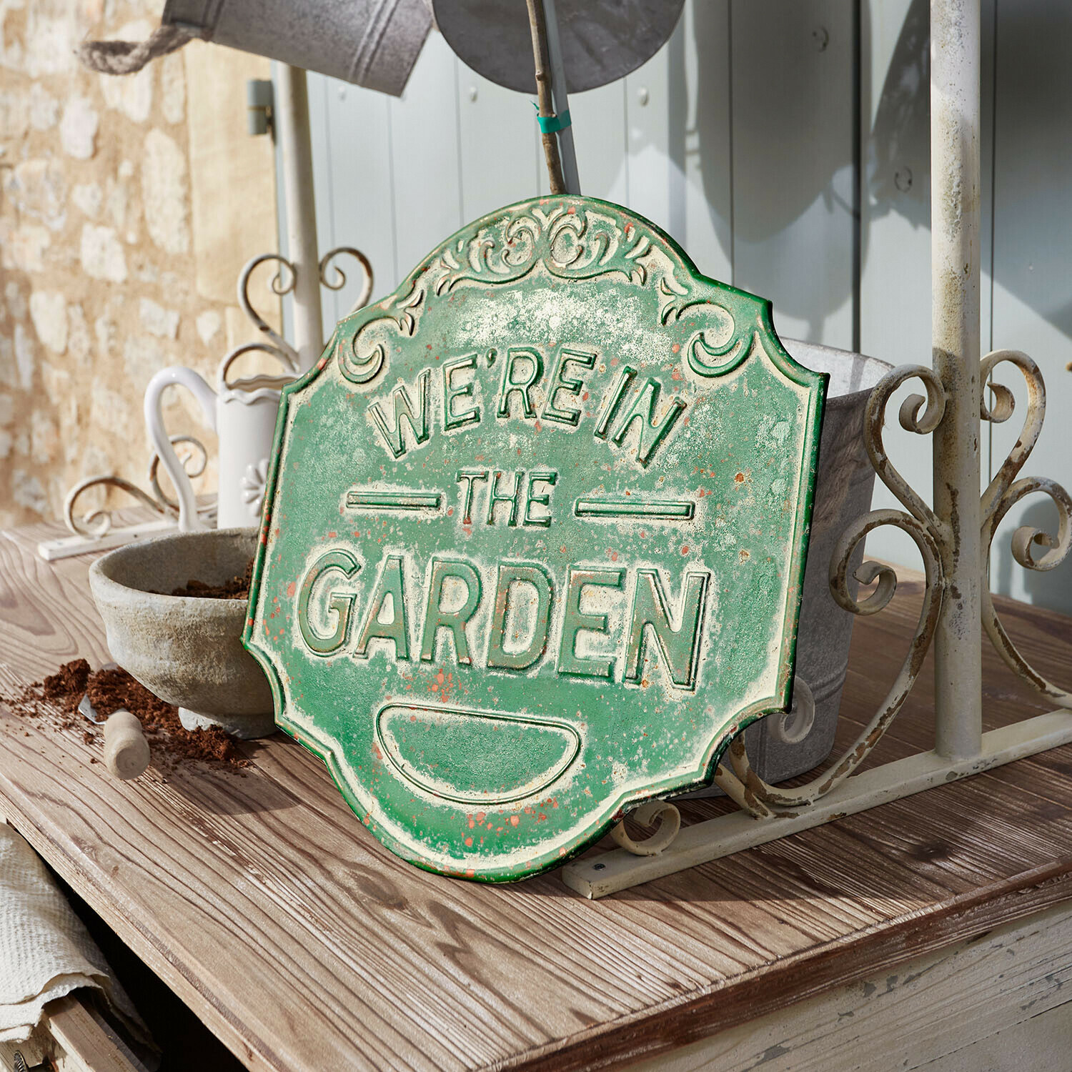 Tablero decorativo Merrin Cartel decorativo de metal verde con texto We're in the Garden sobre mesa de madera en jardín