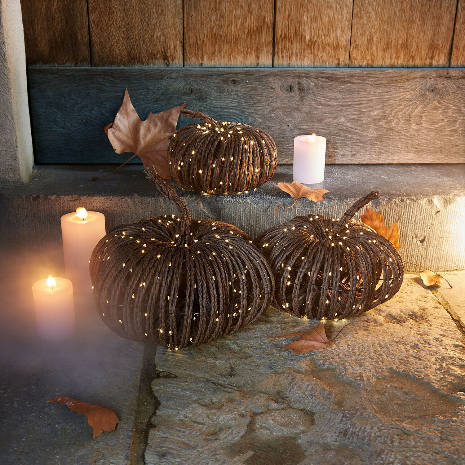 Set de 3 calabazas LED Ysolann Calabazas decorativas de cuerda oscura con luces LED suaves y velas sobre suelo de piedra rústica