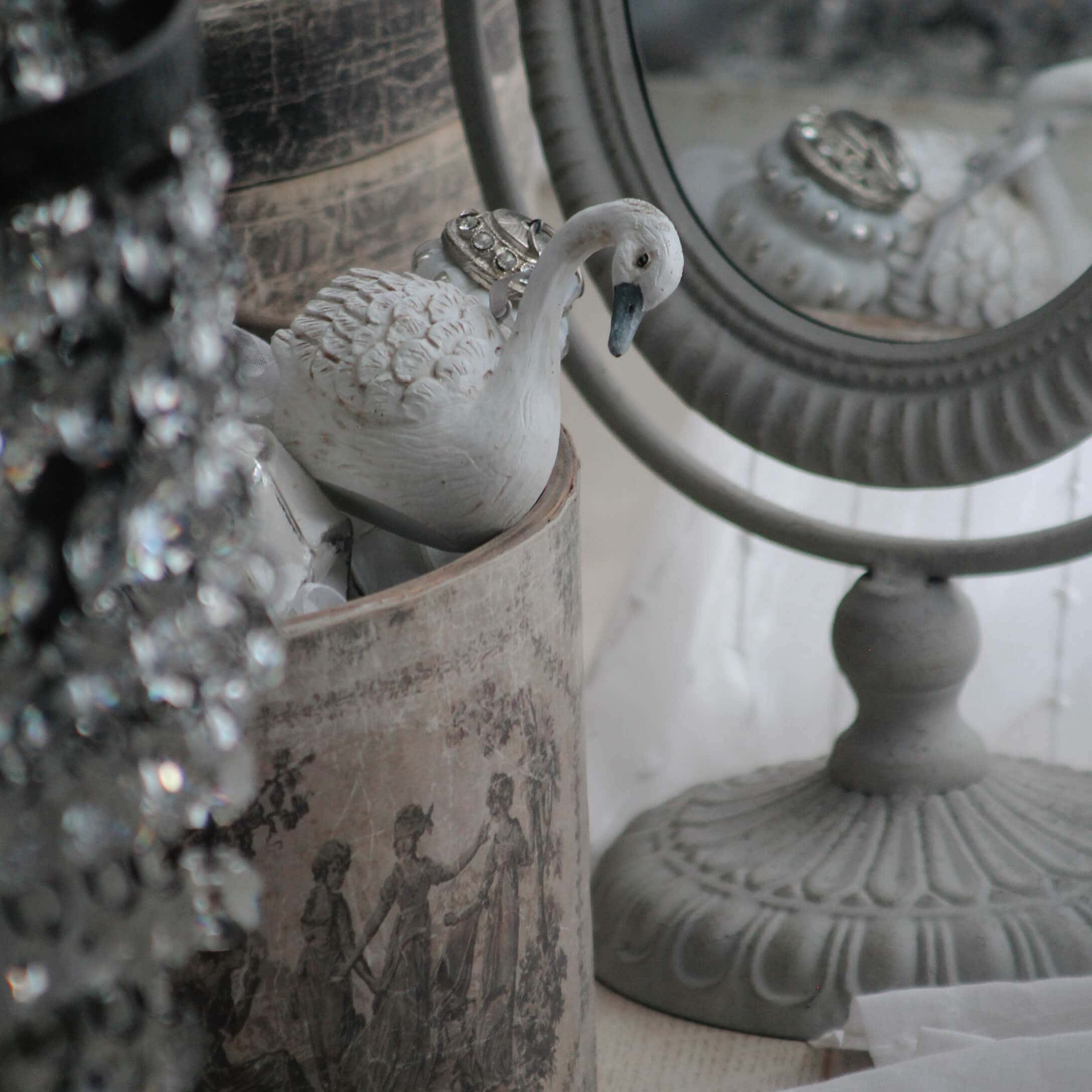 Figura de cisne blanca de cerámica junto a un espejo decorativo y un recipiente vintage con diseño clásico