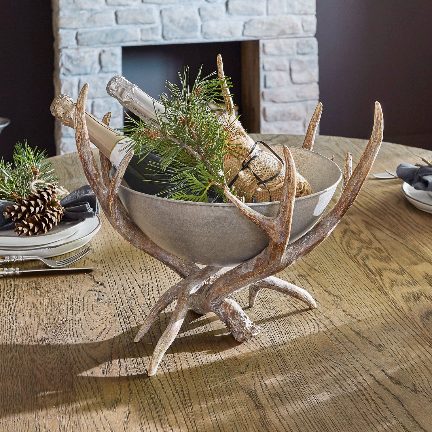 Cuenco decorativo Morlaix Cuenco decorativo de cerámica gris sobre soporte de astas con botellas y ramas verdes sobre mesa de madera