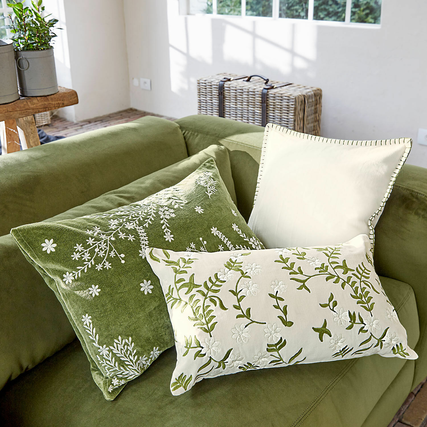 Set de 3 fundas de cojín Iplique Conjunto de tres cojines decorativos bordados en tonos verdes y crema sobre sofá verde