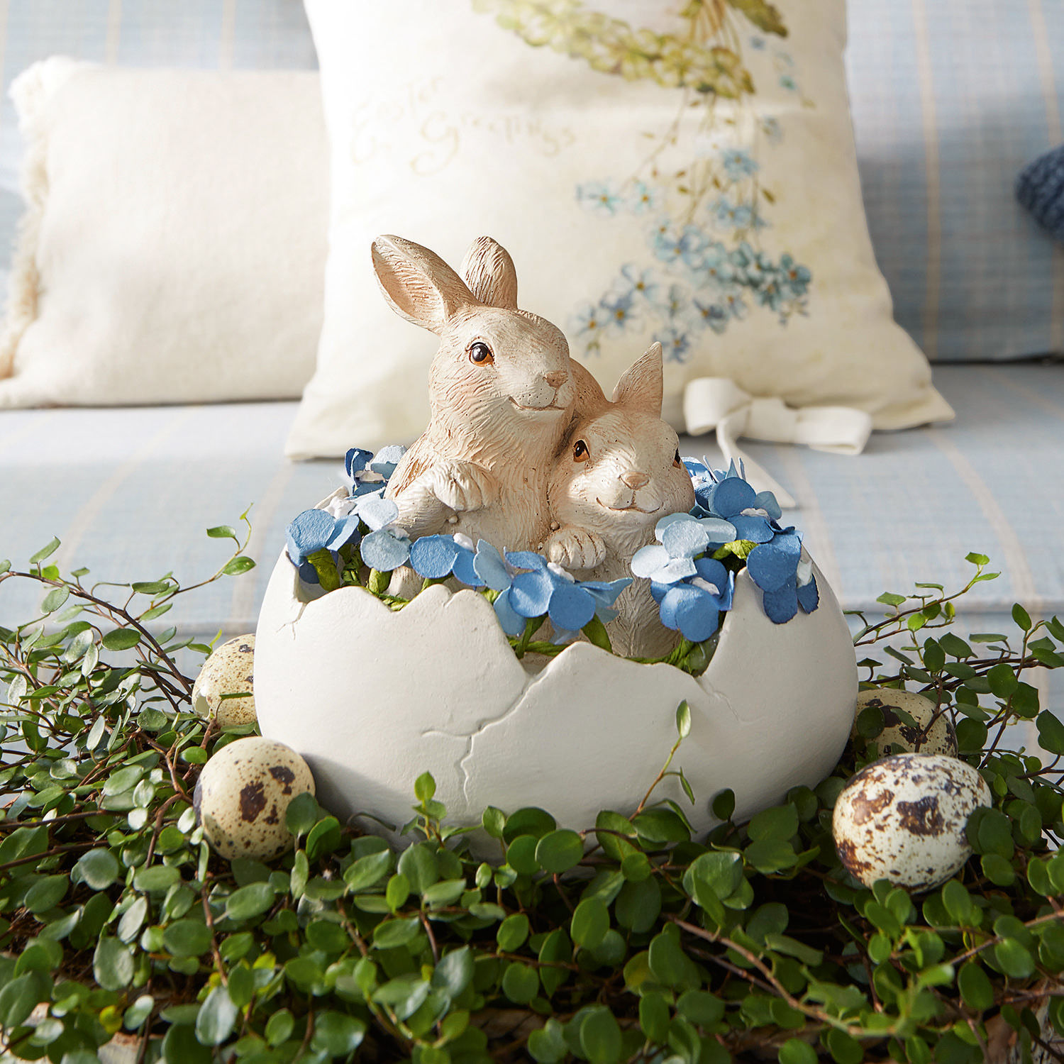 Decoración con dos conejos en cáscara de huevo blanca, flores azules y hojas verdes