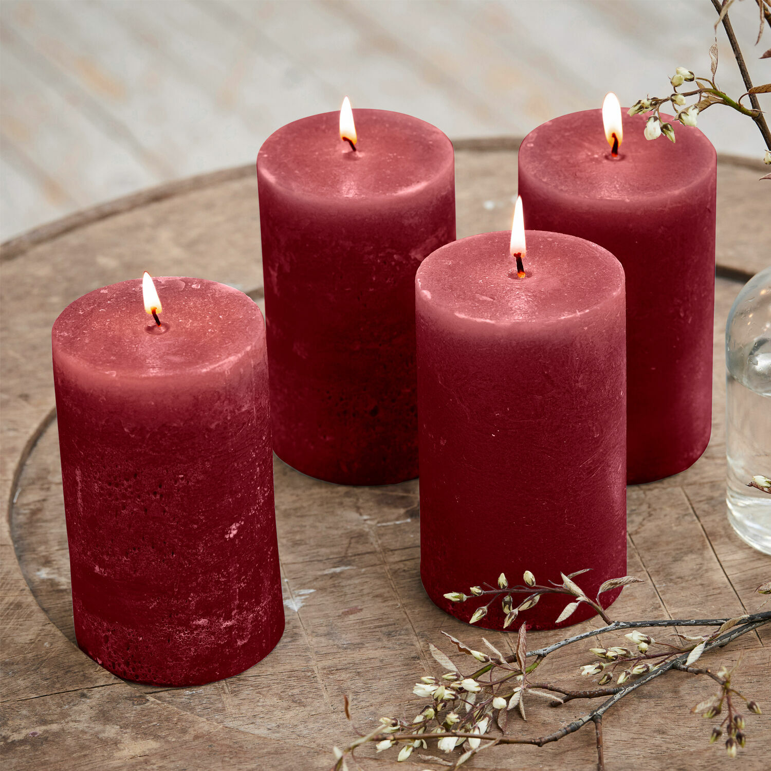 Cuatro velas rojas de cera sobre mesa de madera con decoración floral, ambiente acogedor