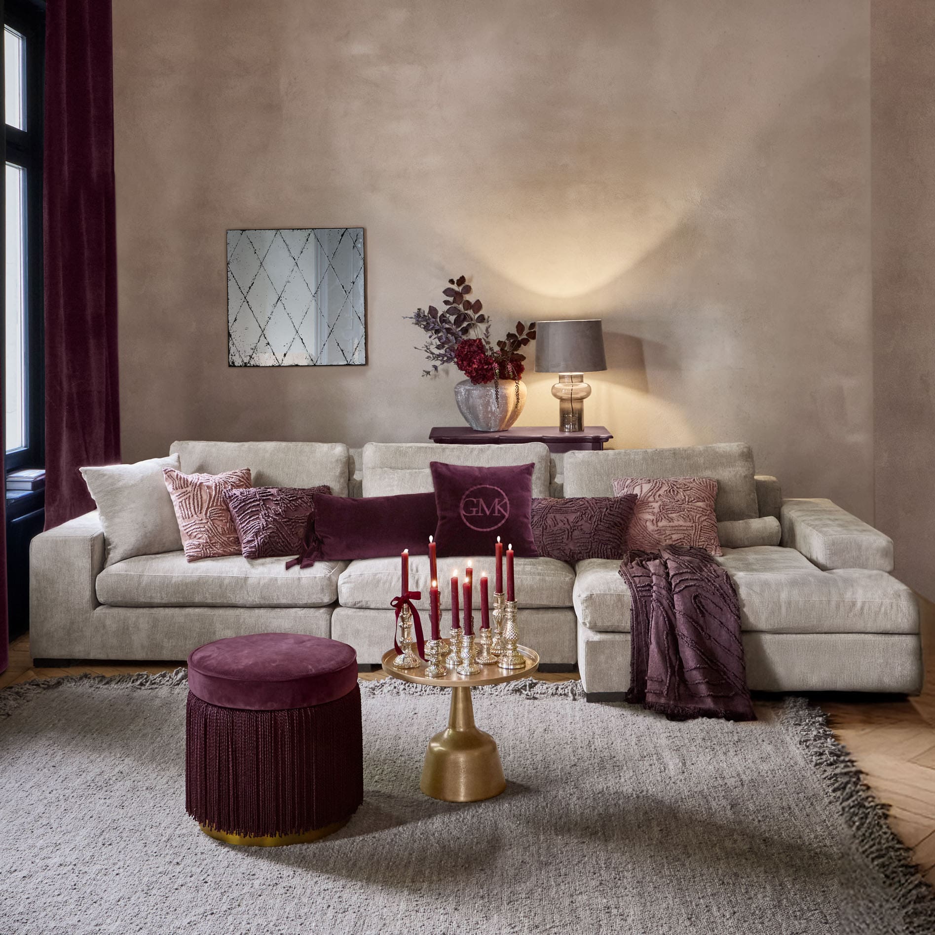 Sala acogedora con sofá beige, cojines burdeos y mesa dorada con velas rojas