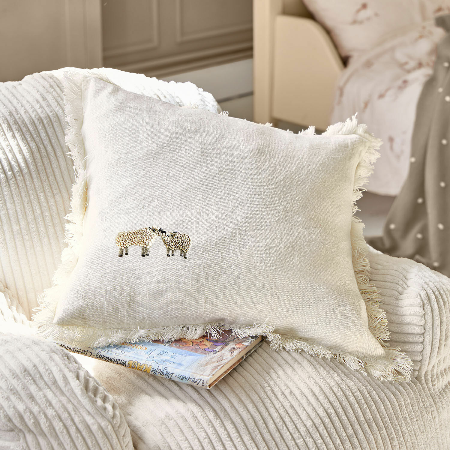 Funda de cojín Erianna Cojín beige de lino con flecos y bordado de ovejas sobre sillón suave, decoración hogar