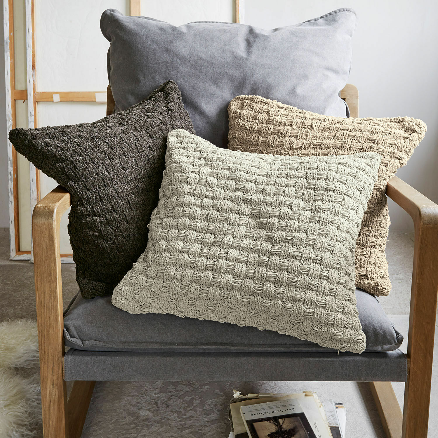 Set de 3 fundas de cojín Antier Conjunto de tres cojines decorativos de tejido trenzado en tonos beige y marrón sobre sillón gris