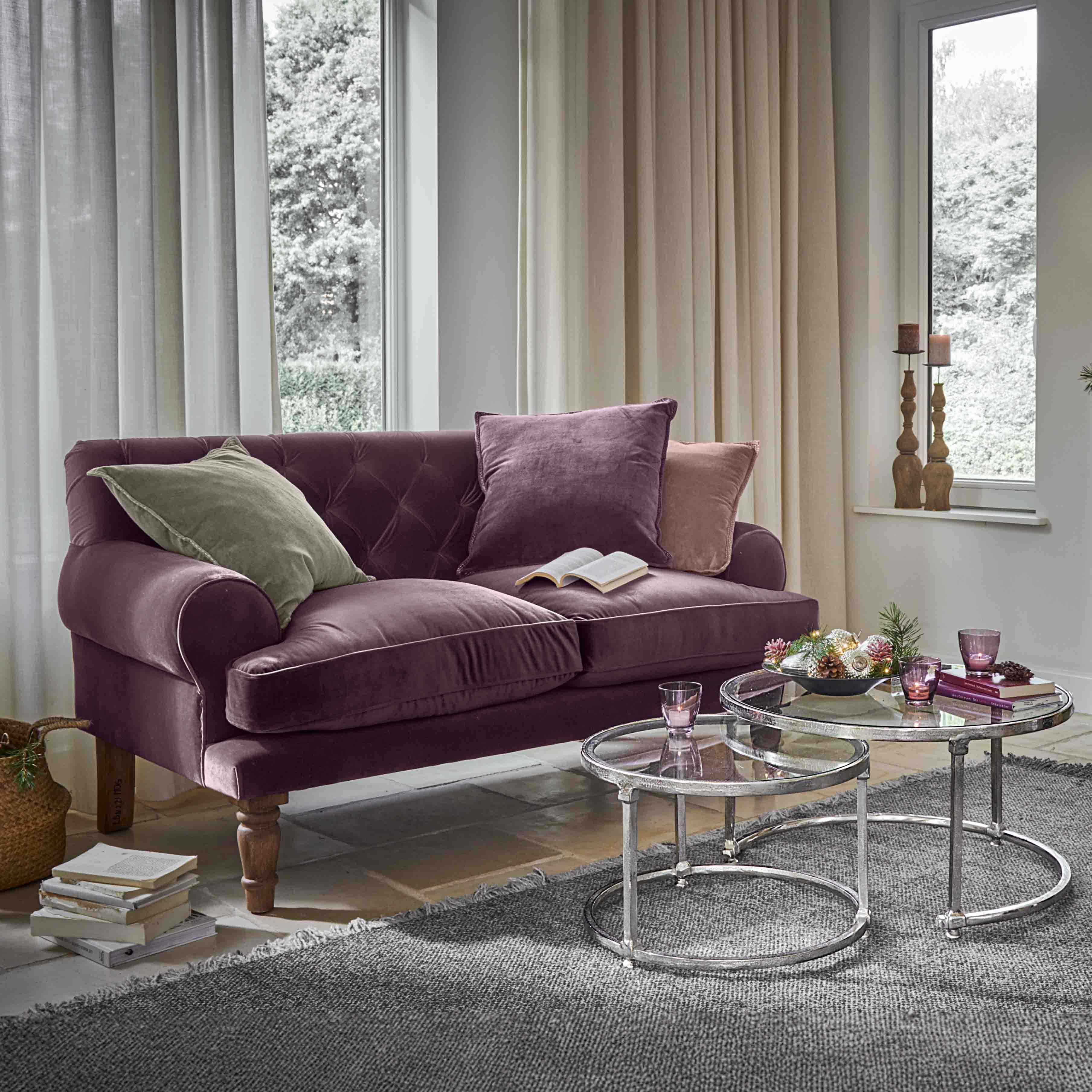 Sofá de terciopelo morado con cojines y mesas de centro de cristal en sala luminosa