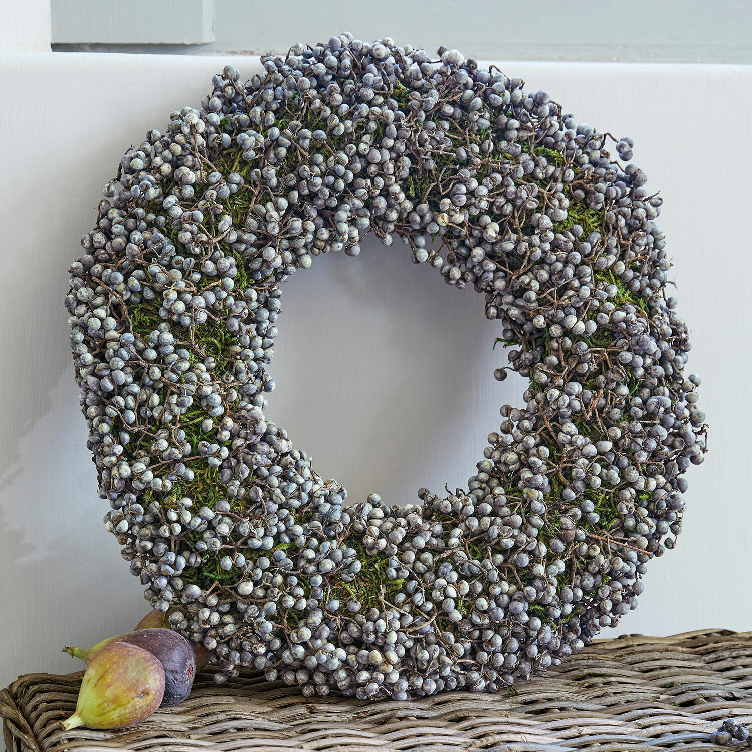 Corona Elly Corona decorativa de bayas secas y musgo verde sobre mesa de mimbre, decoración de temporada