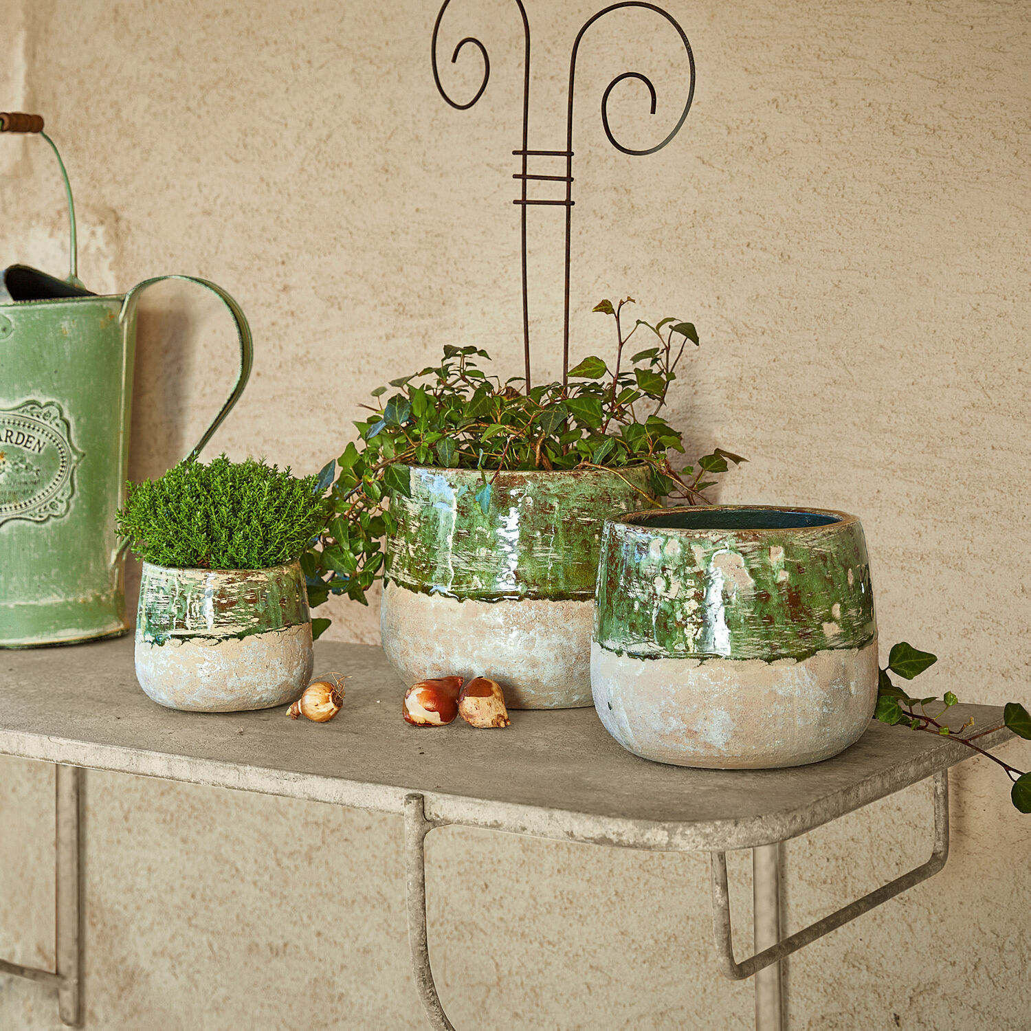 Conjunto de tres macetas de cerámica verde y beige en estante metálico para decoración de jardín