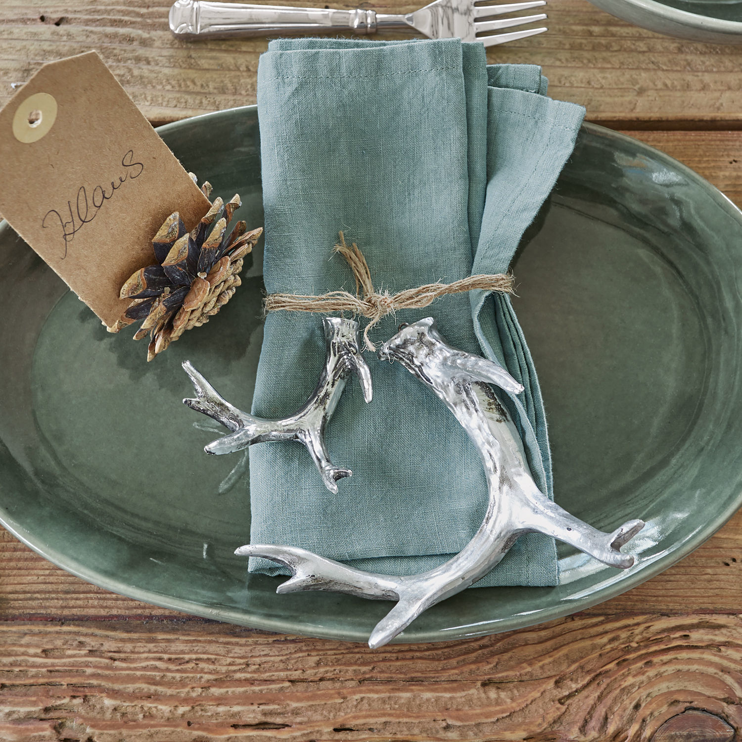 Set de 2 cornamentas decorativas Tiana Fuente de cerámica verde con servilleta de lino y adornos plateados en forma de cuernos sobre mesa de madera