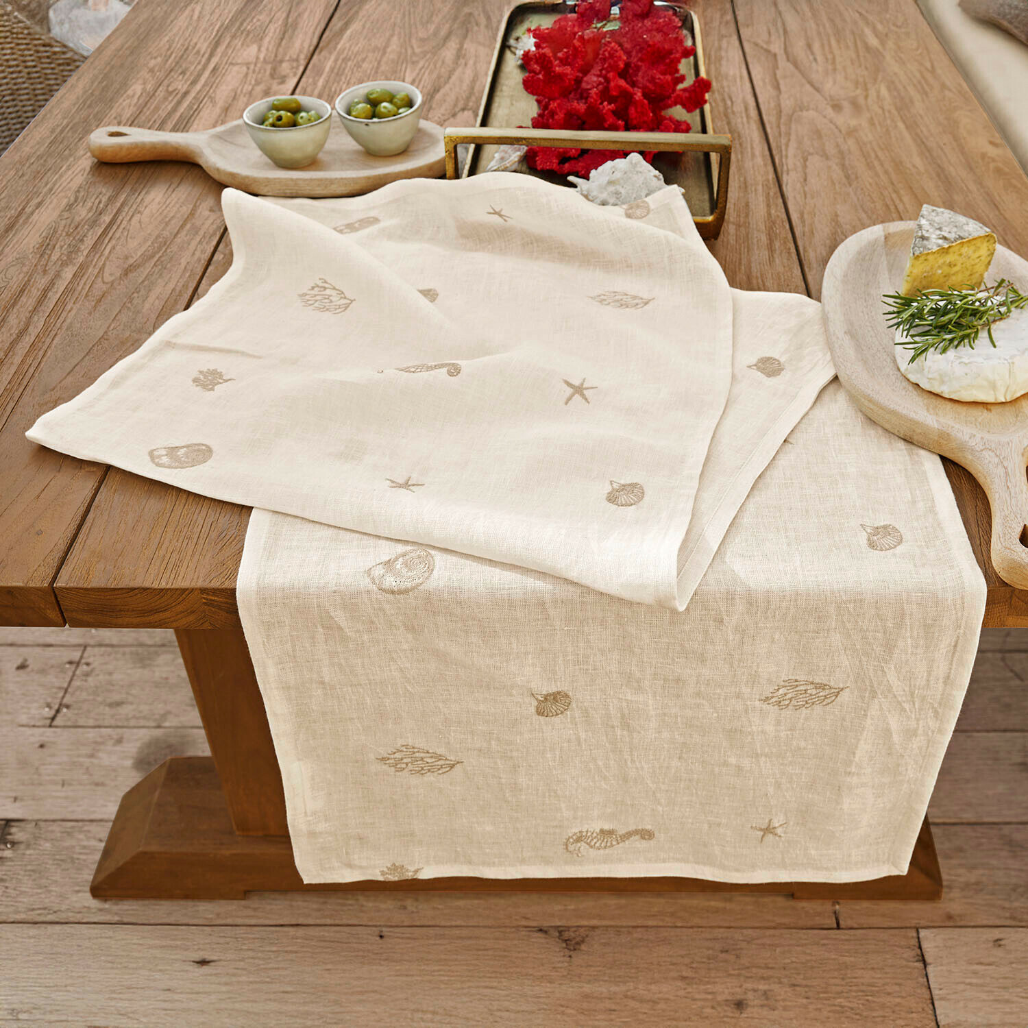 Camino de mesa Celorin Camino de mesa de lino color natural con motivos marinos bordados sobre mesa de madera para decoración