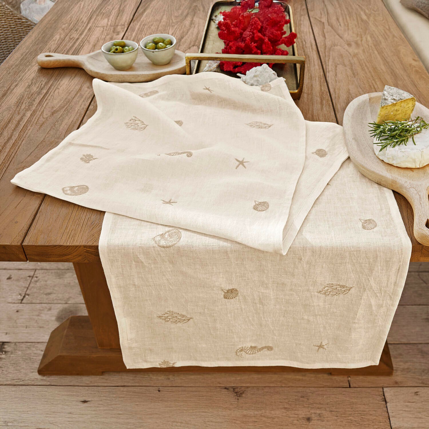 Camino de mesa Celorin Camino de mesa de lino color natural con motivos marinos bordados sobre mesa de madera para decoración