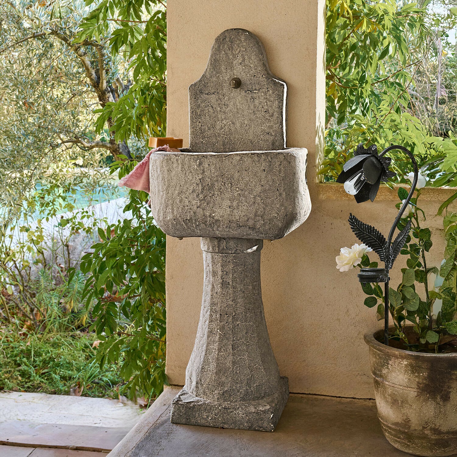 Fuente Lurevino Lavabo de jardín de piedra gris sobre columna con acabado natural y plantas verdes alrededor
