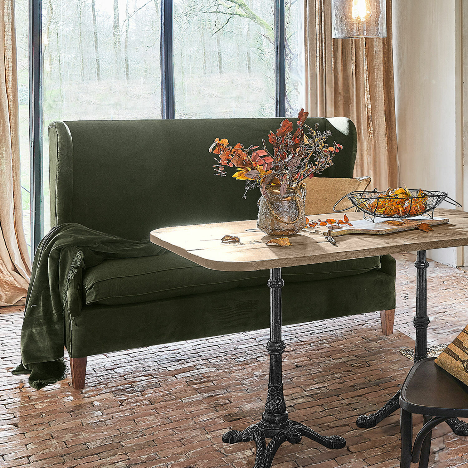 Sofa Ombra Sofá verde de terciopelo junto a mesa de madera con patas metálicas en sala luminosa con suelo de ladrillo