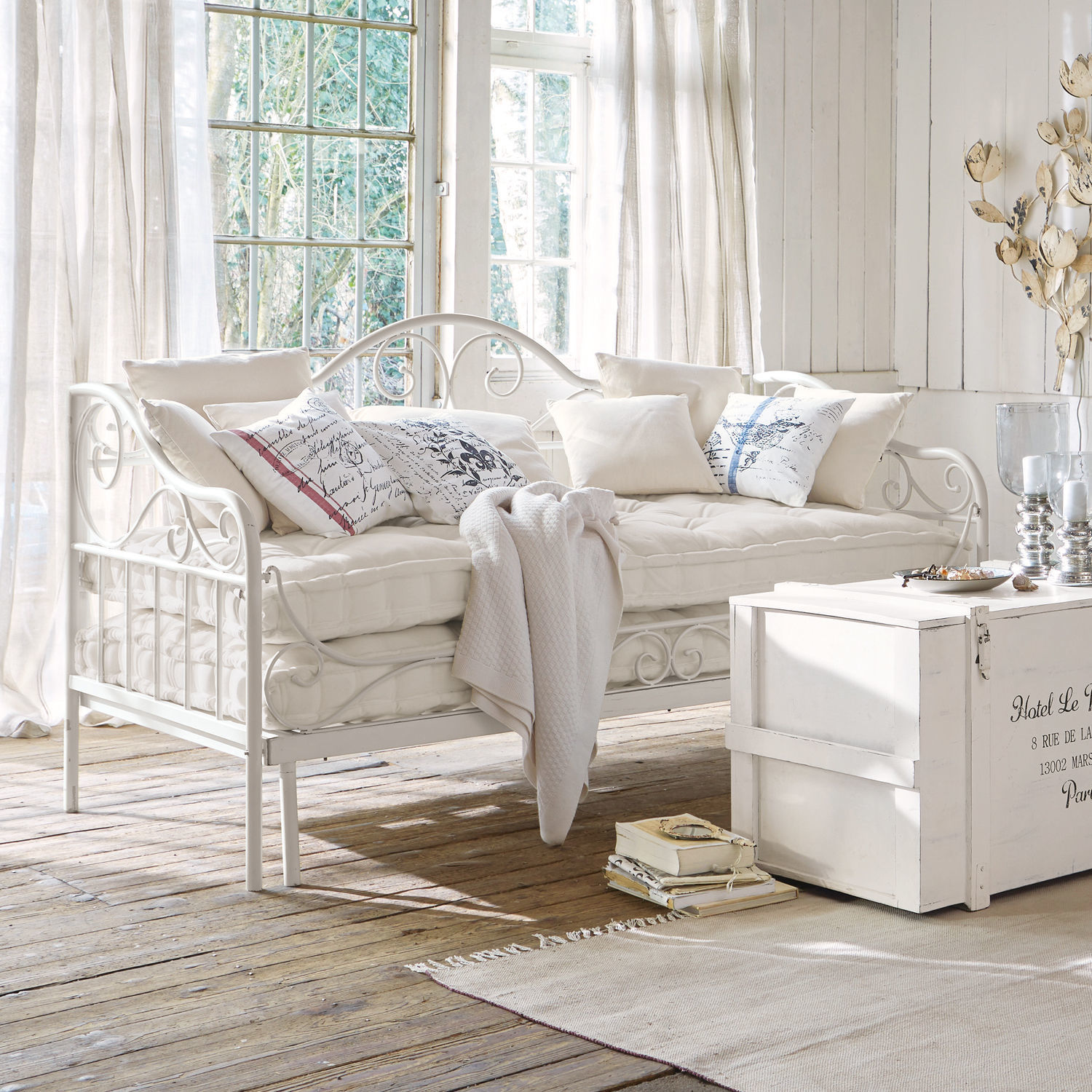 Sofá cama Maditha Sofá metálico blanco con cojines suaves y manta en interior luminoso con suelo de madera natural