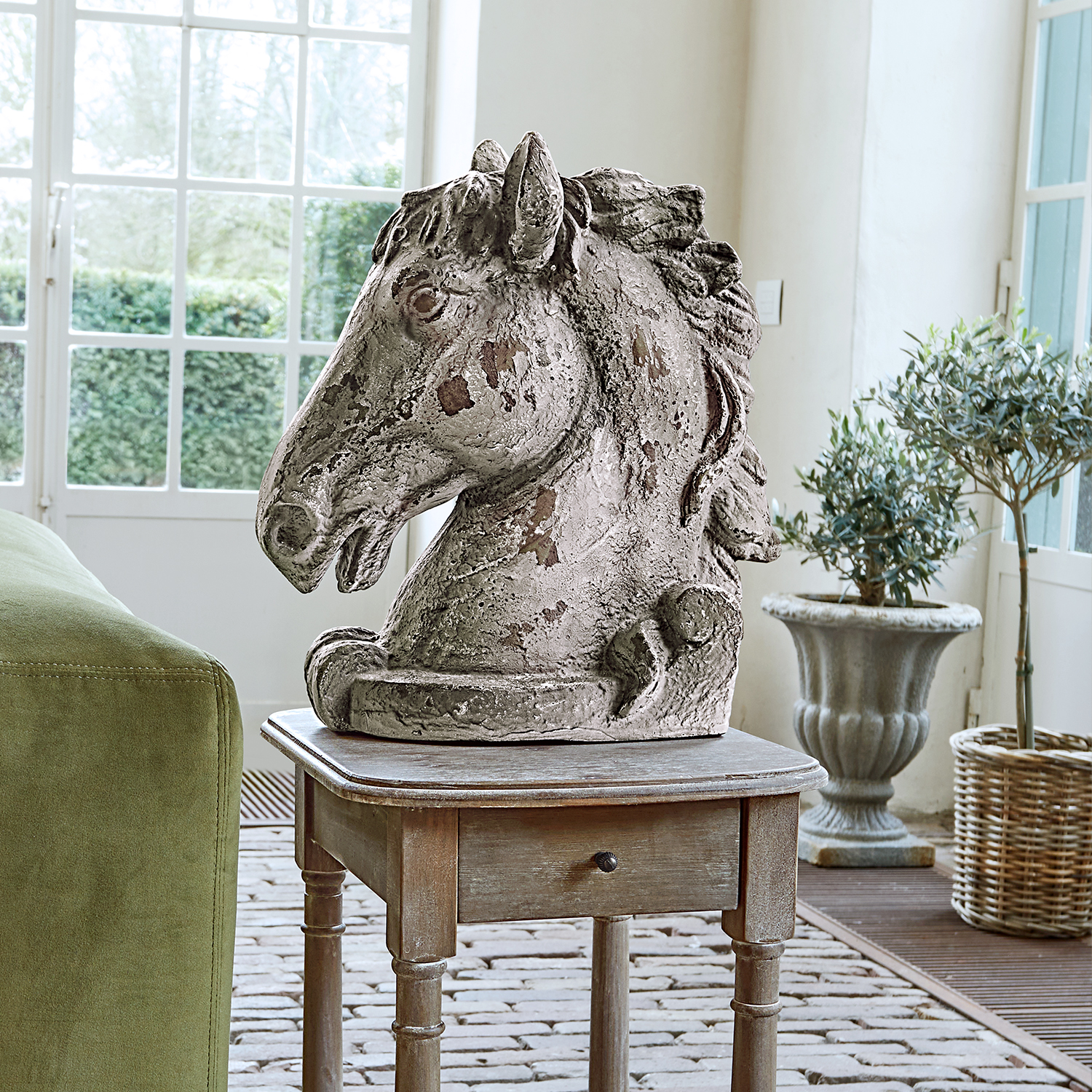Escultura de cabeza de caballo en hormigón envejecido gris sobre mesa de madera en interior luminoso
