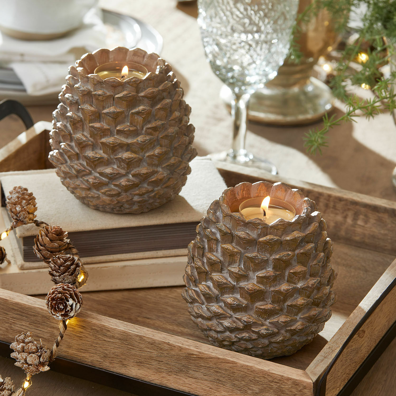 Set de 2 portavelas Butz Dos portavelas de resina marrón con forma de piña sobre una bandeja de madera, decoración de mesa