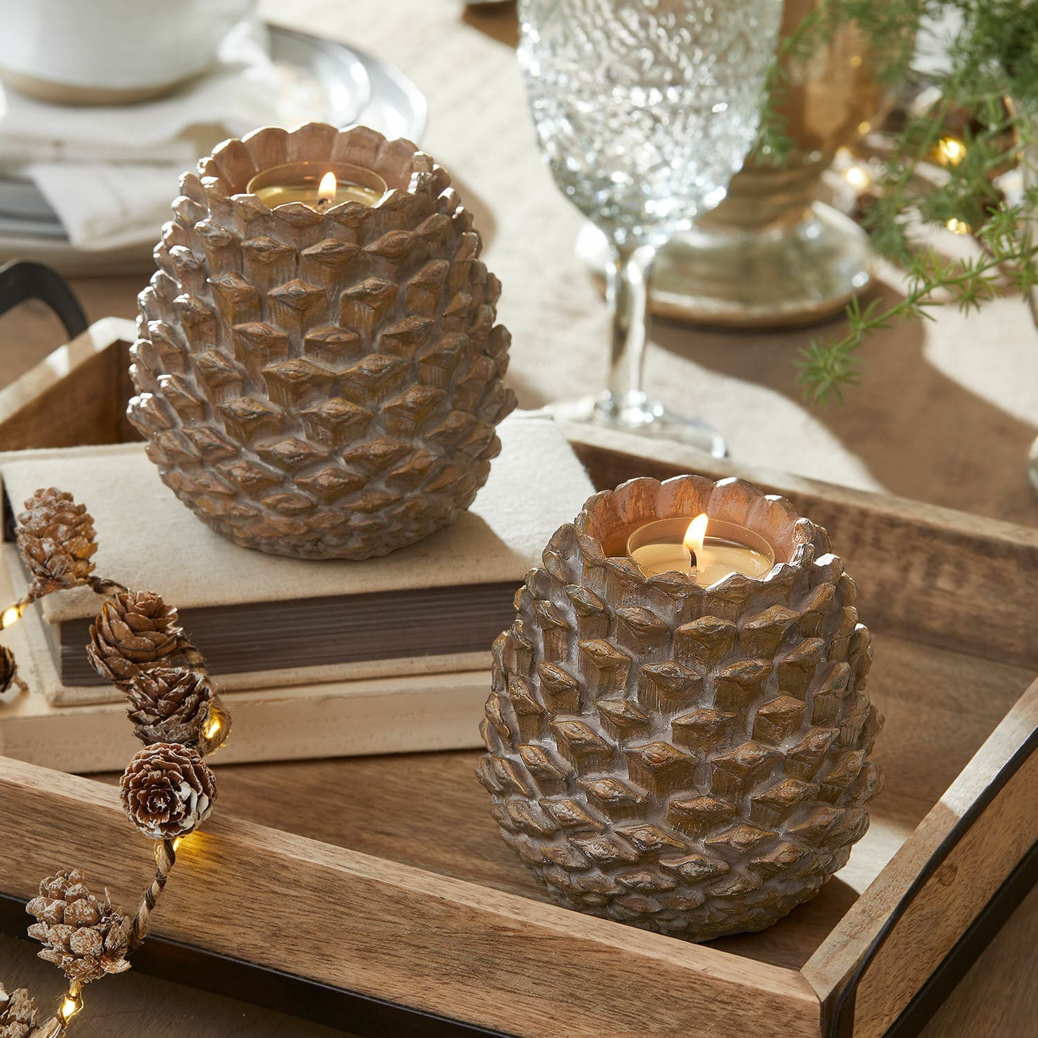 Set de 2 portavelas Butz Dos portavelas de resina marrón con forma de piña sobre una bandeja de madera, decoración de mesa