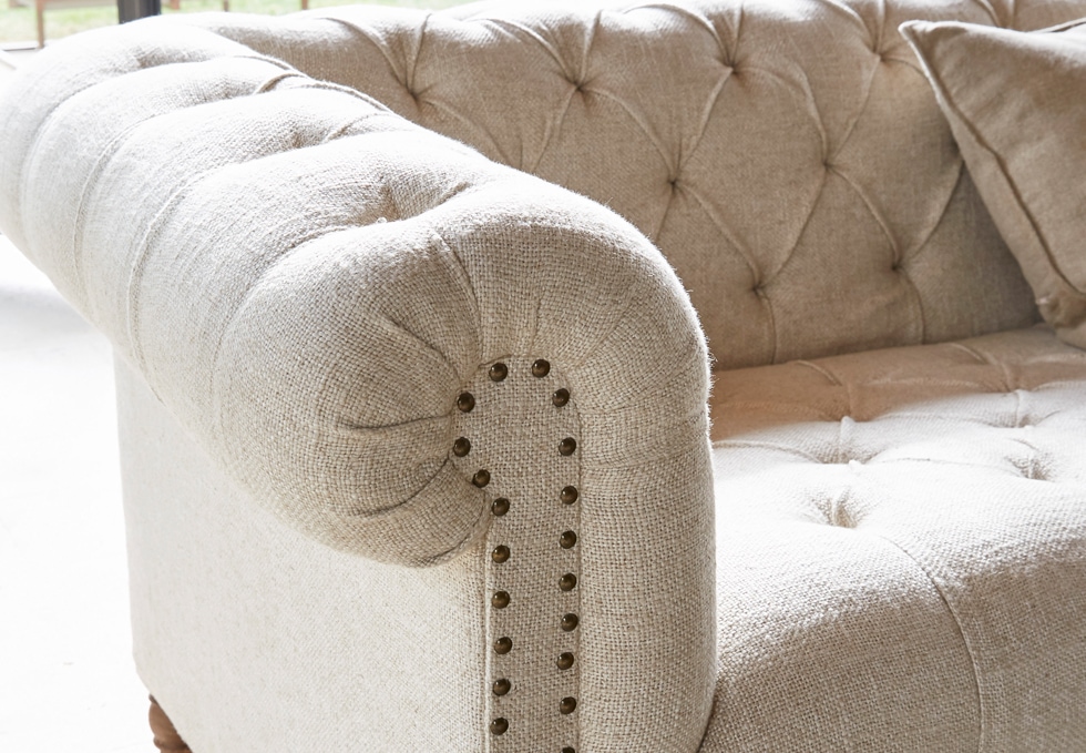 Sofá clásico beige de tela con respaldo capitoné y clavos decorativos para sala elegante