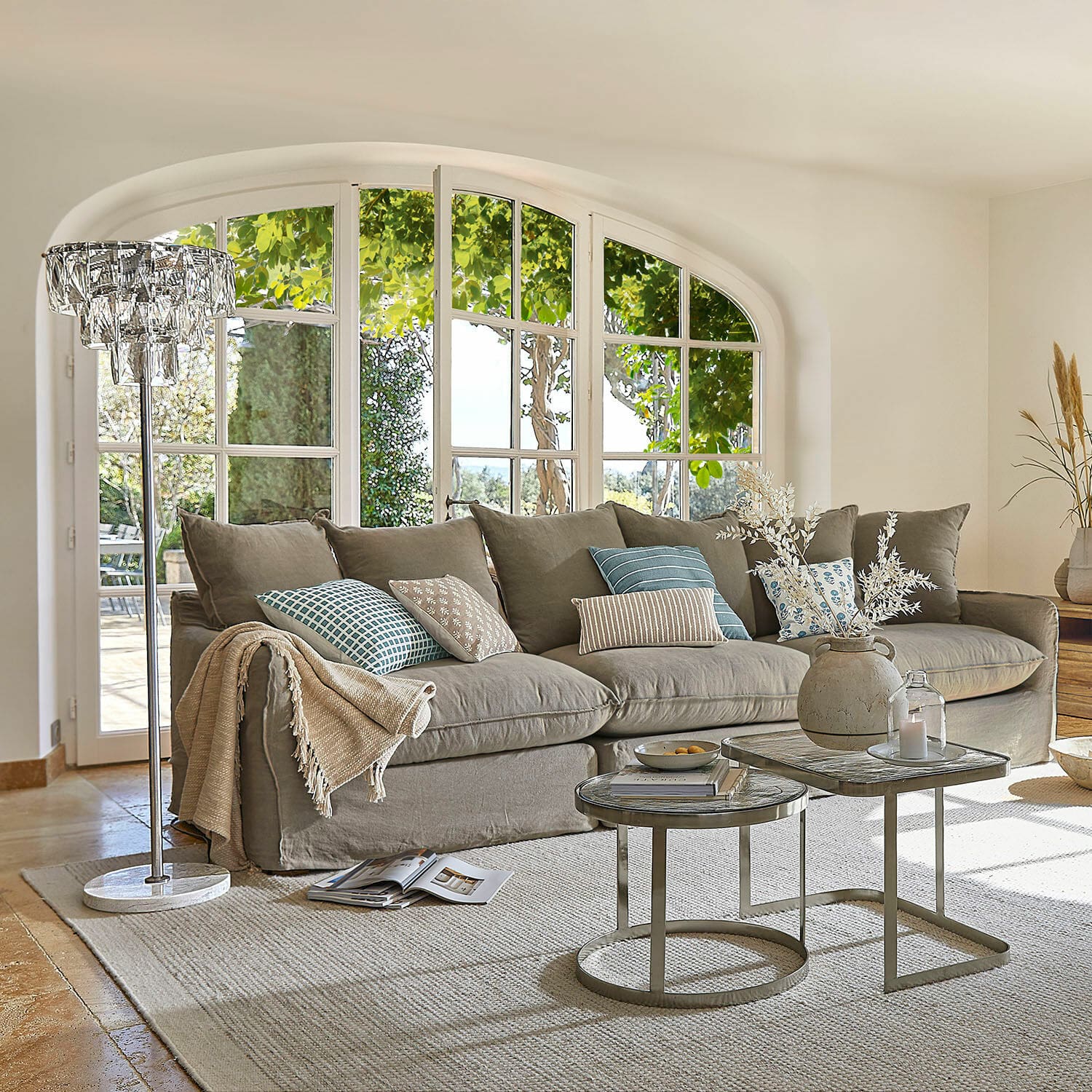 Sofá Finchingfield Sofá gris acogedor con cojines y mesas auxiliares en sala luminosa con grandes ventanas