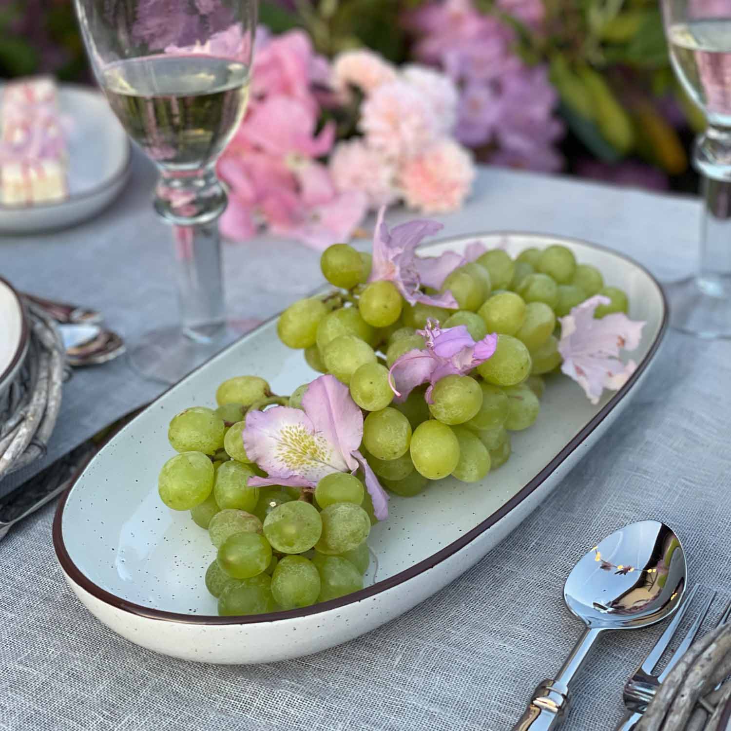 Uvas verdes con flores rosas en plato de cerámica blanca sobre mantel gris
