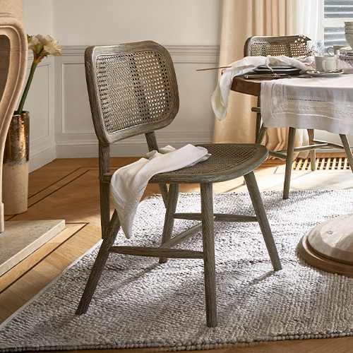Silla de madera y ratán en color natural sobre alfombra en salón luminoso con mesa puesta