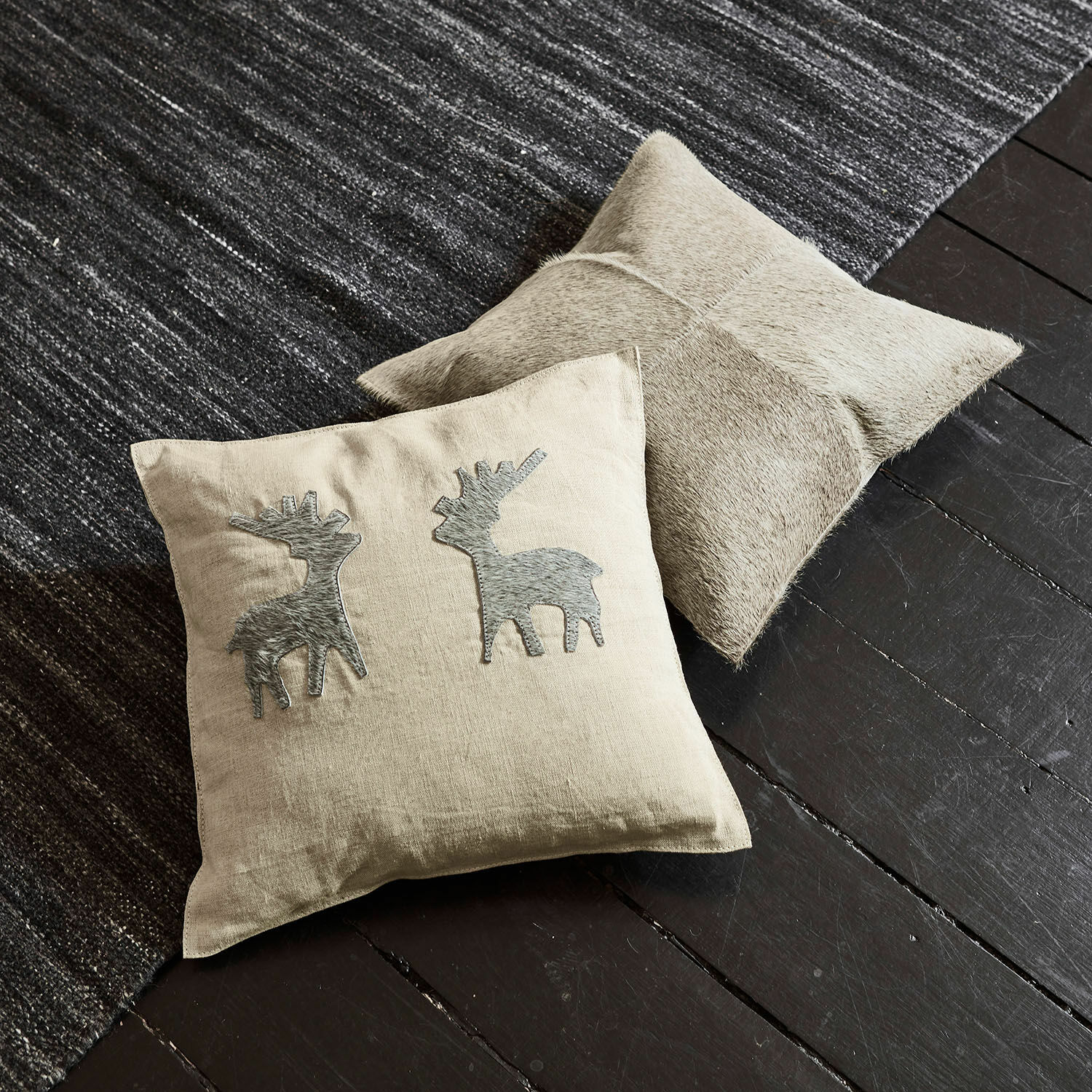 Set de 2 fundas de cojín Beaupuy Cojín beige de lino con aplicaciones de ciervos grises y cojín de cuero claro sobre suelo oscuro y alfombra