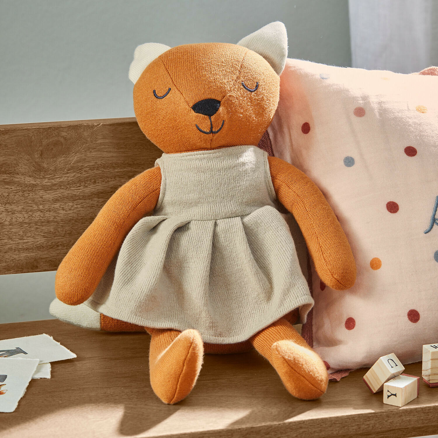 Peluche Fuzzlin Peluche de zorro naranja con vestido beige sentado en banco de madera con cojín y bloques de madera