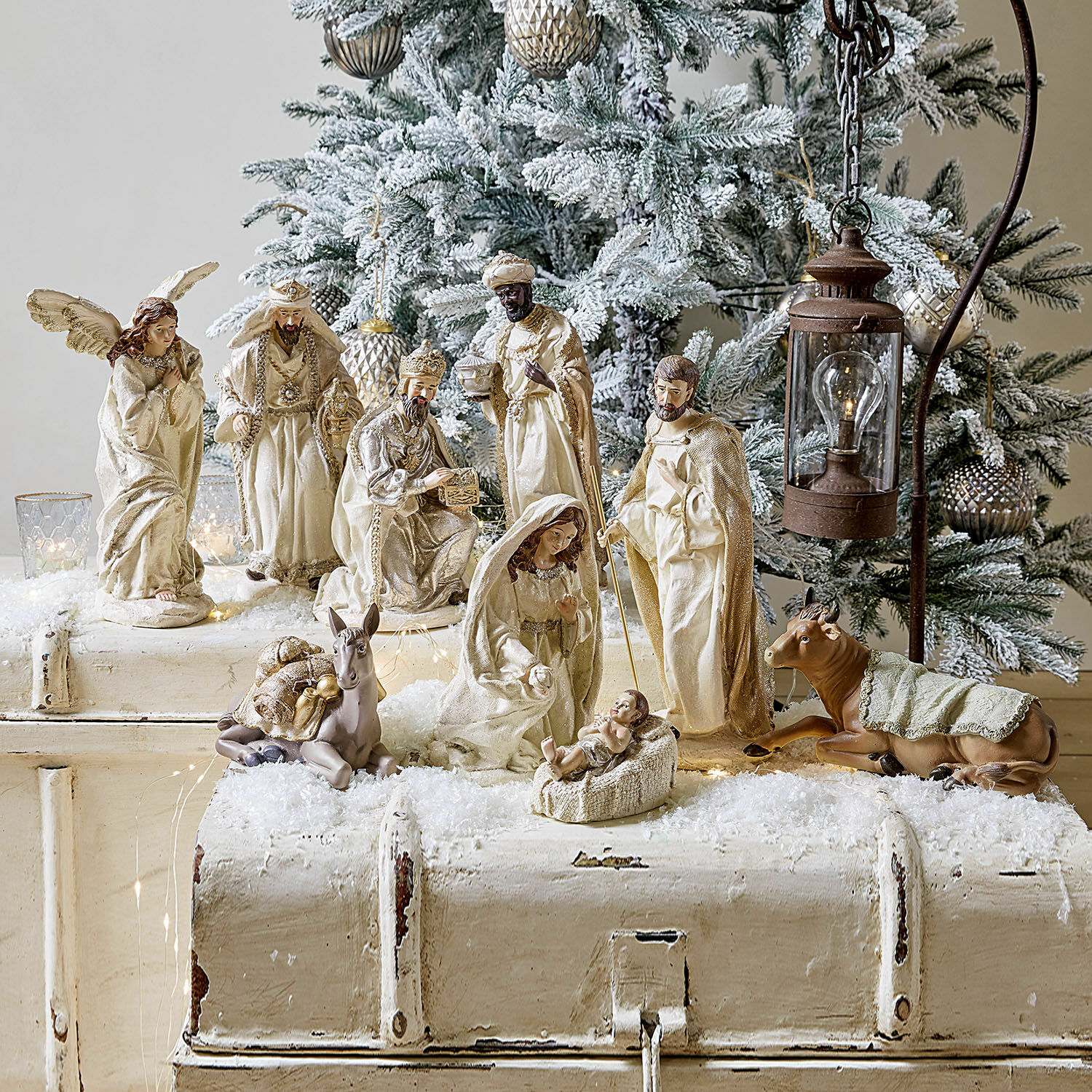Set de 9 figuras Liré Figuras de belén en tonos crema frente a árbol de Navidad nevado y farol decorativo
