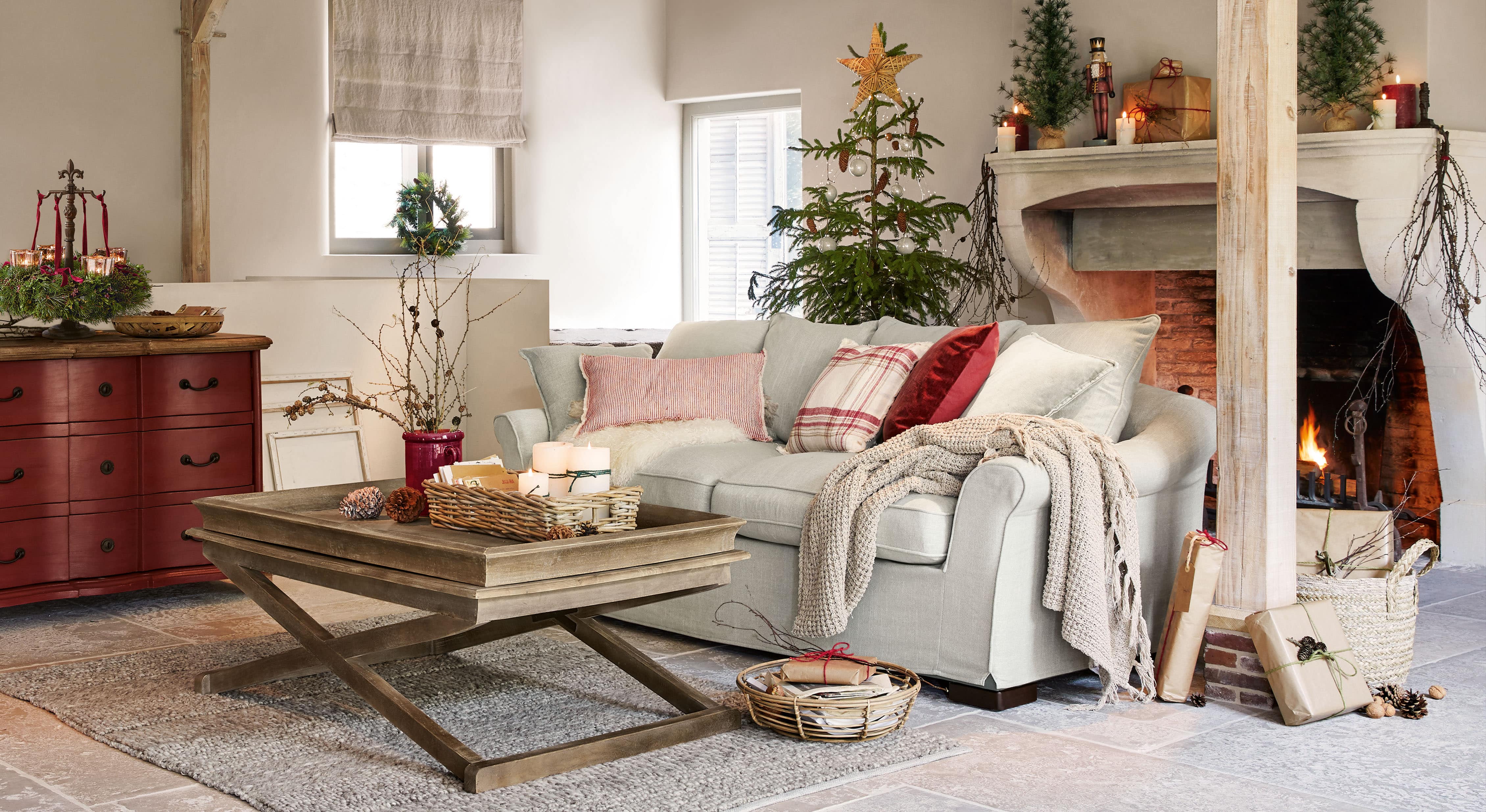 Salón acogedor con sofá gris claro, mesa de centro de madera y decoración navideña con árbol y chimenea encendida