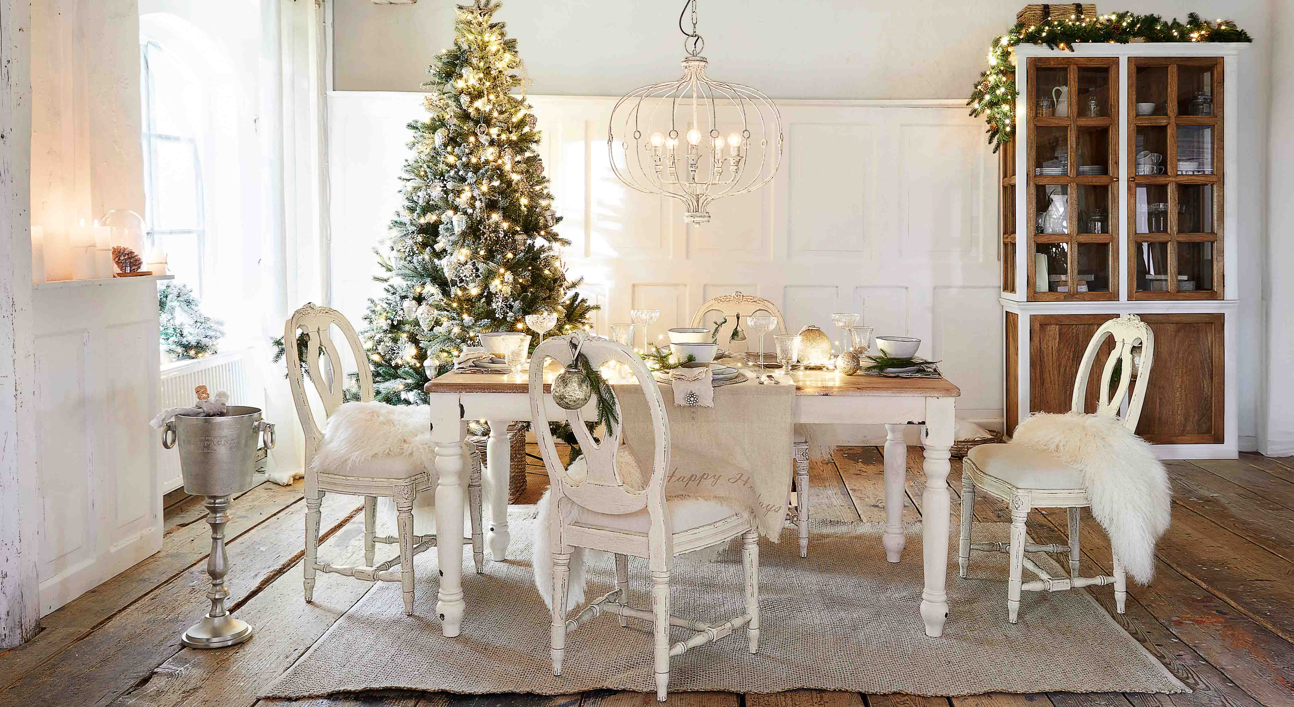 Comedor con mesa y sillas de madera blanca decorado para Navidad con árbol y luces festivas